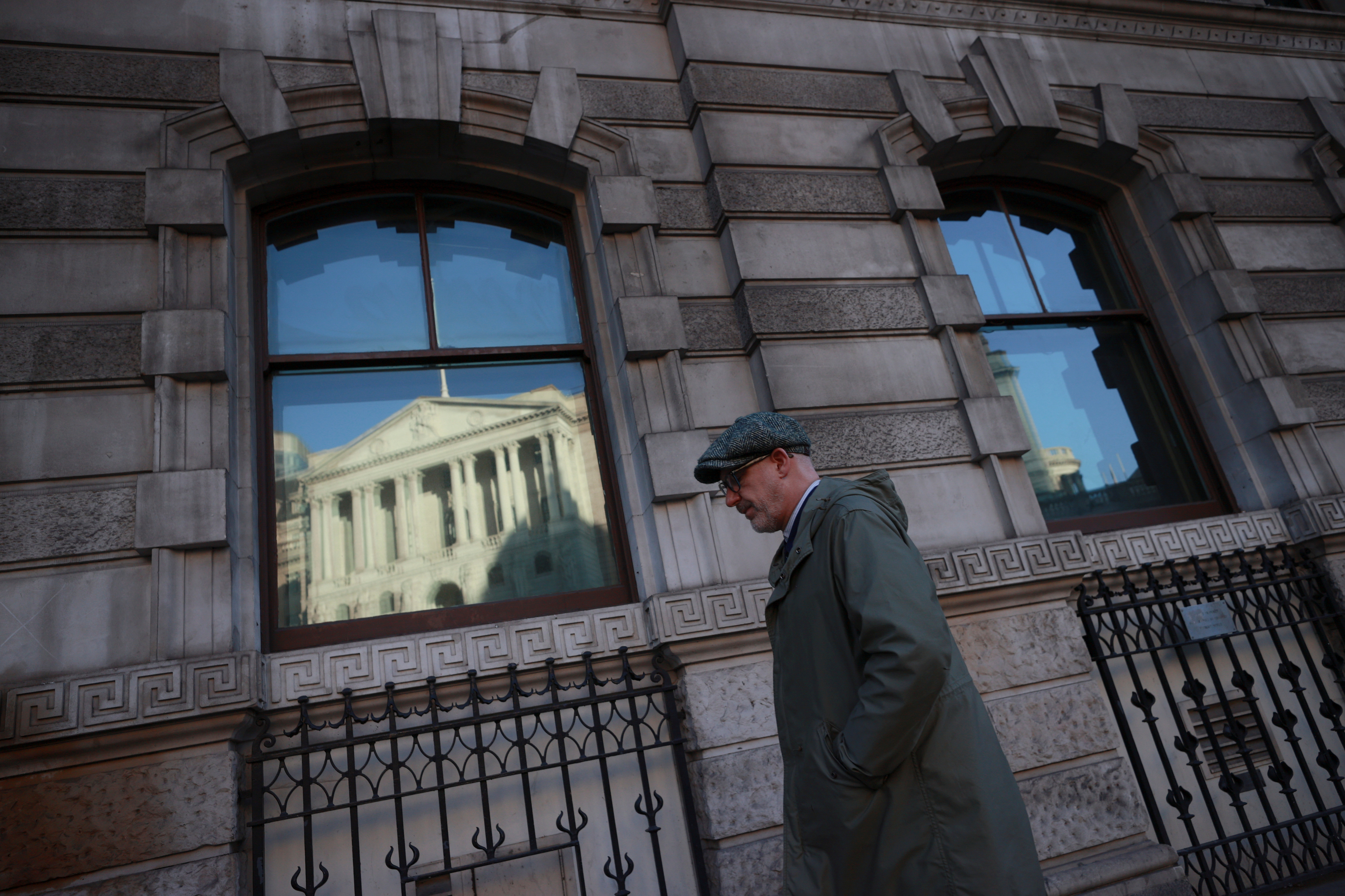 A man walks past a window reflecting the Bank of England, in London