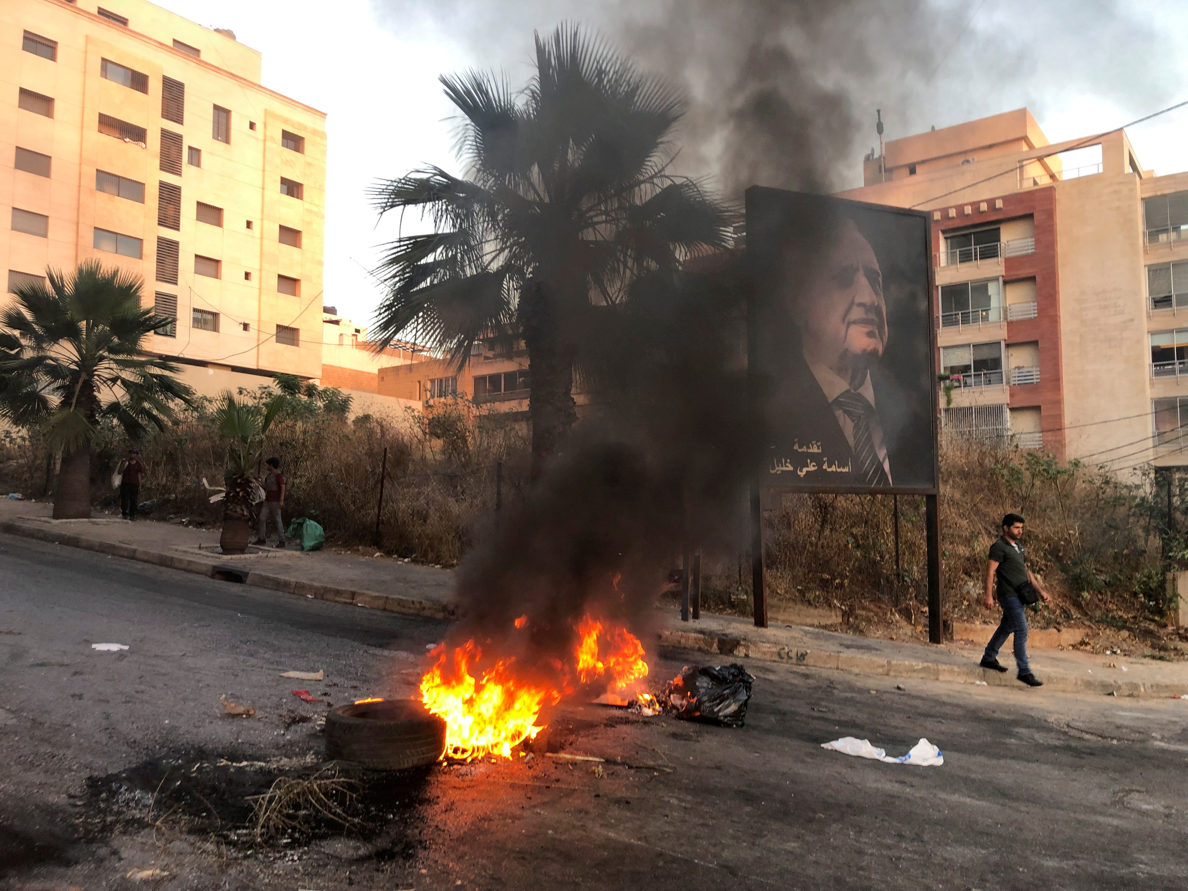 A man walks near a burning fire blocking a road, during a protest against mounting economic hardships, in Beirut
