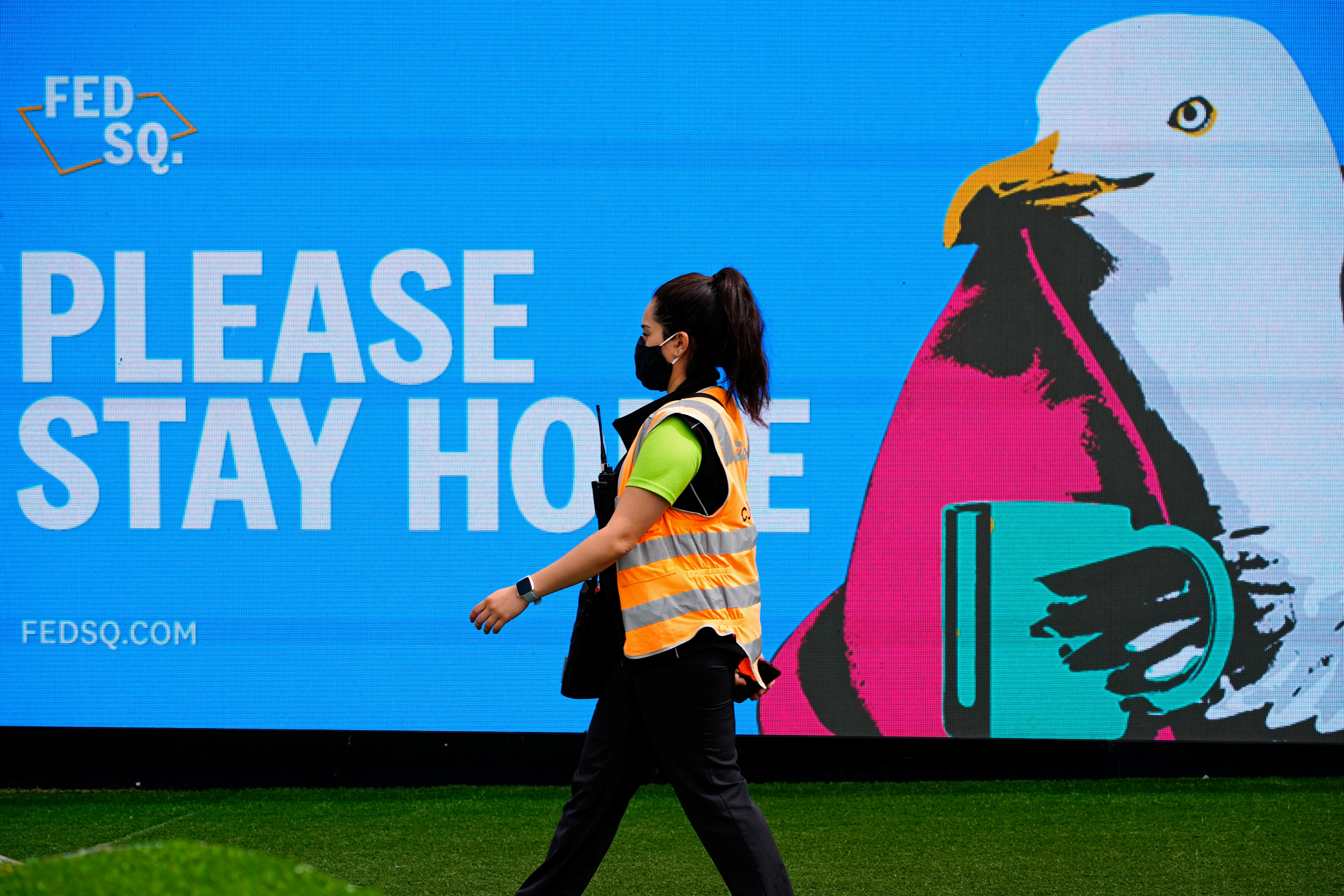 An essential worker walks past a 'Please Stay Home' sign on the first day of a five-day lockdown implemented in the state of Victoria in response to a coronavirus disease (COVID-19) outbreak in Melbourne, Australia, February 13, 2021.  REUTERS/Sandra Sanders