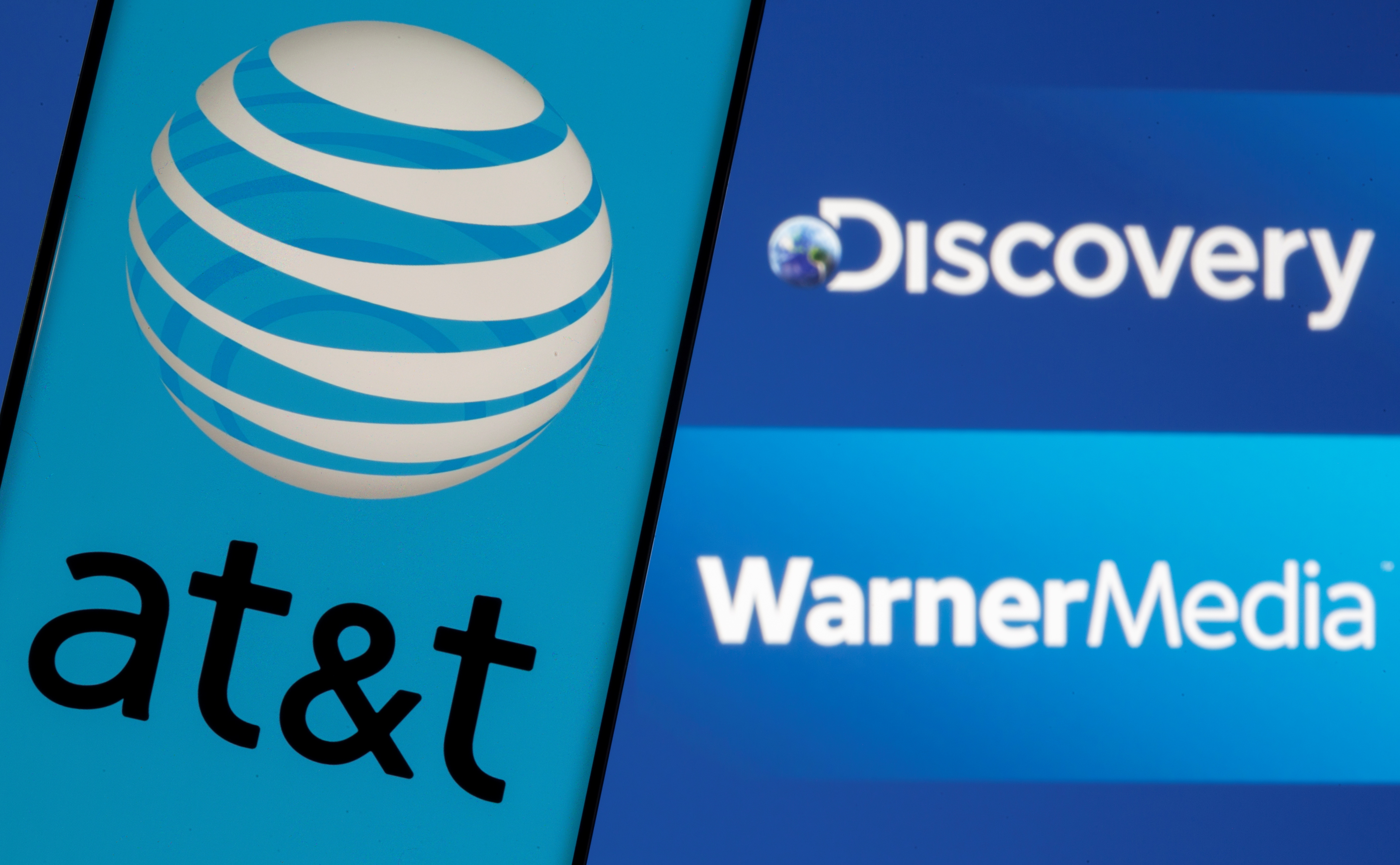 AT&T logo is seen on a smartphone in front of displayed Discovery and Warner Media logos in this illustration