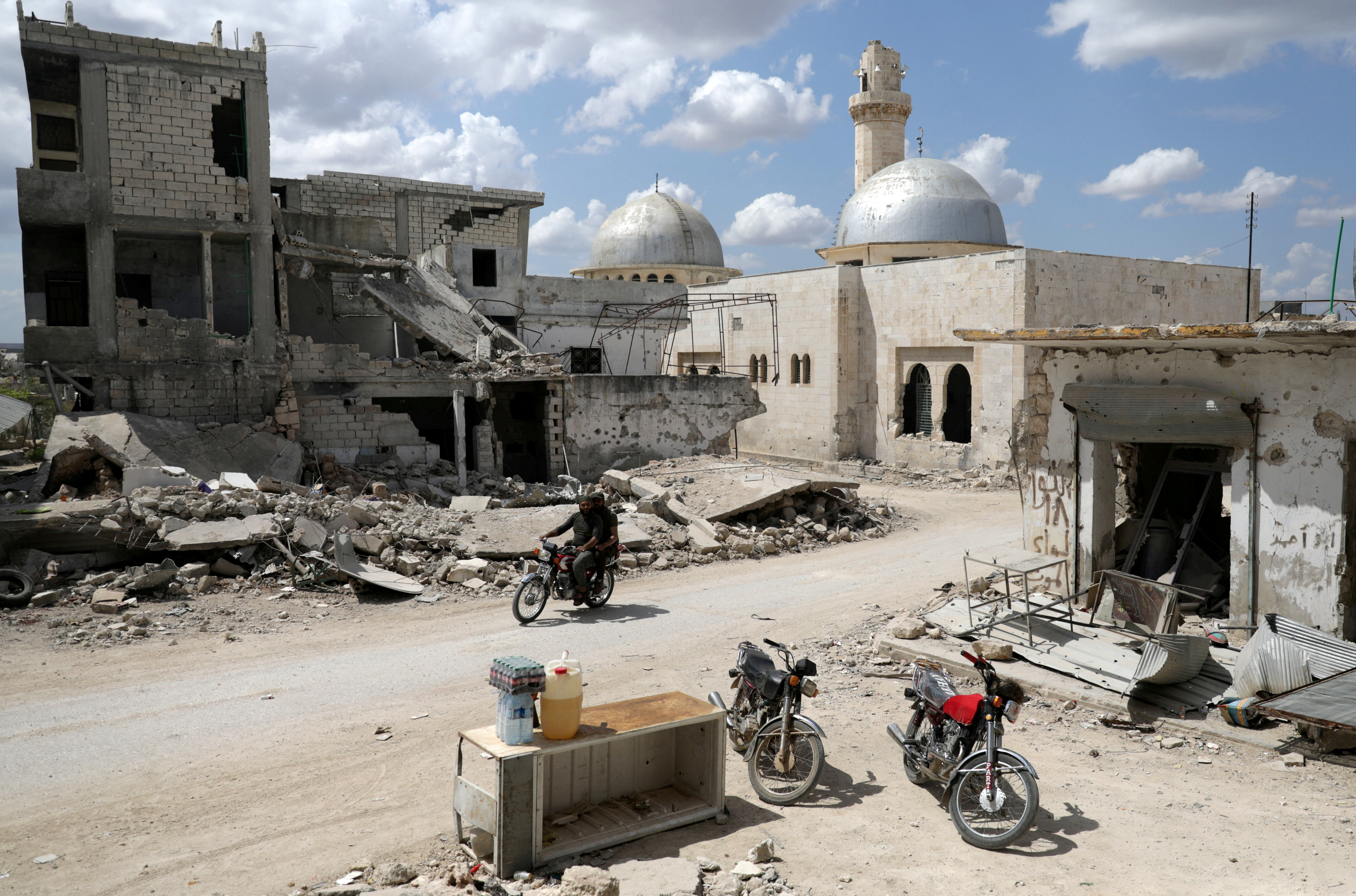 Men ride a motorbike past damaged buildings in the rebel-held town of Nairab
