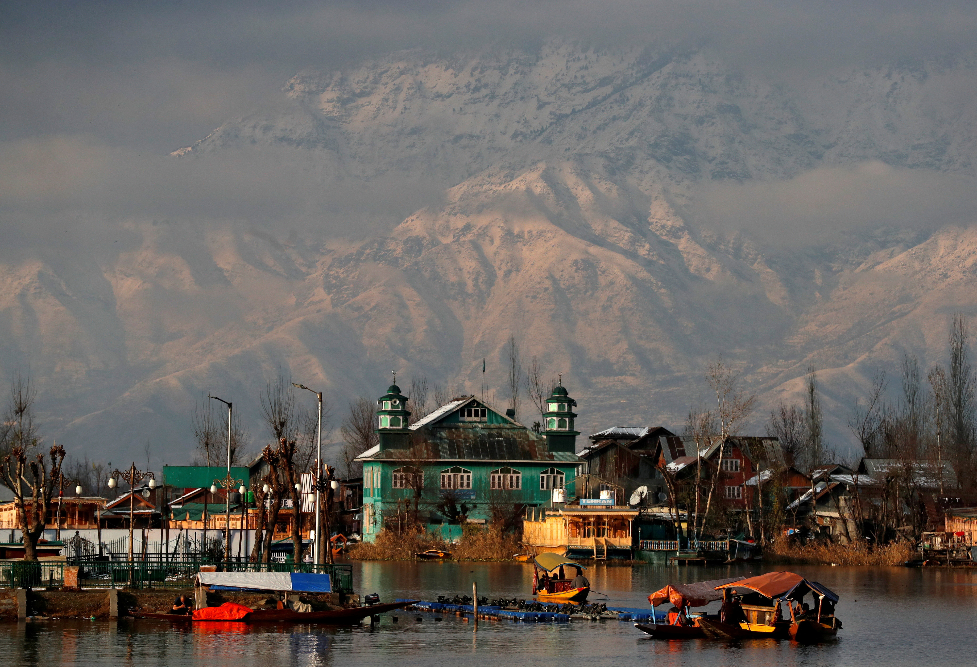 People row their boats in the waters of Dal Lake with the backdrop of snow-covered mountains after a snowfall in Srinagar