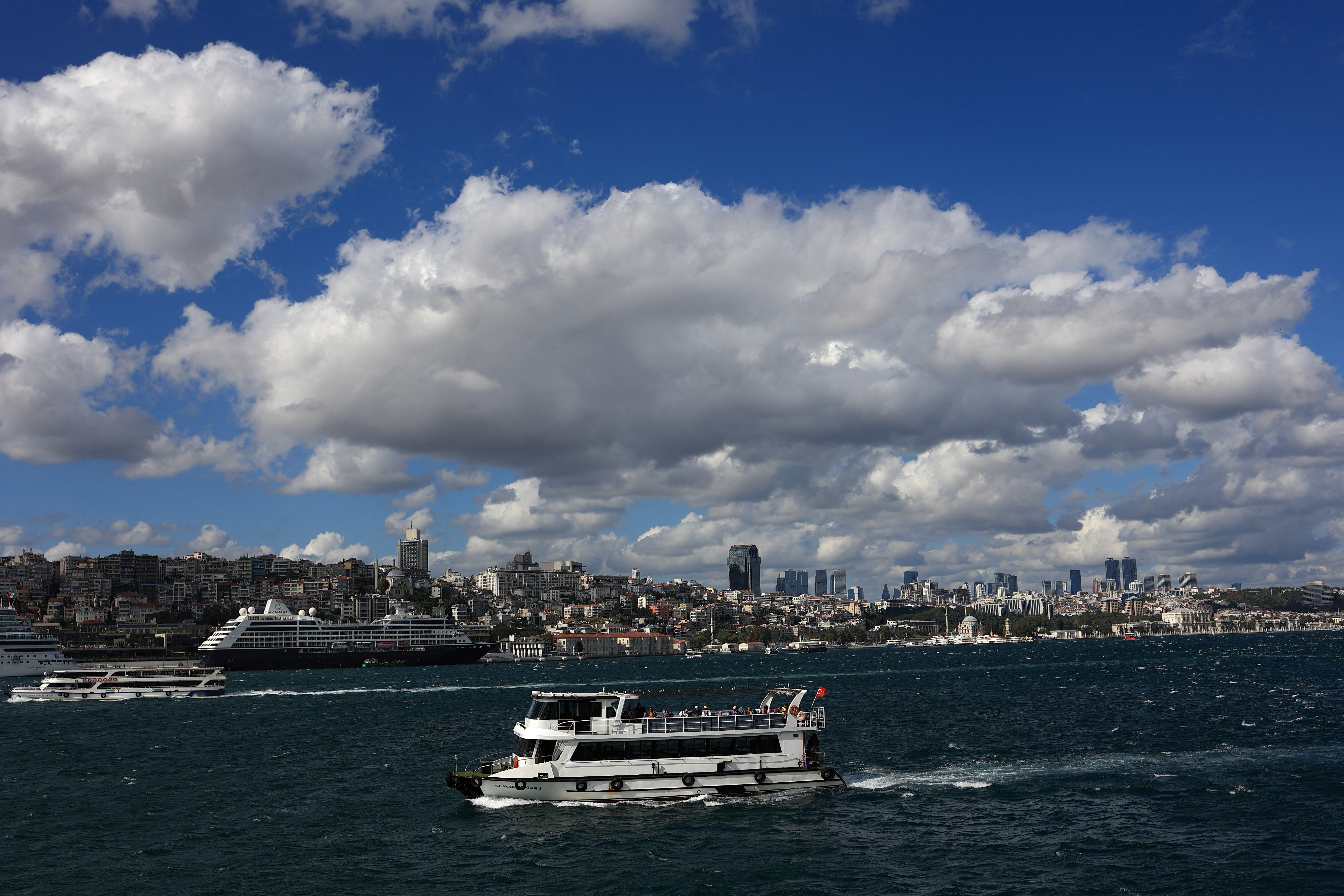 A tourist boat sails in the Bosphorus as the cruise ship Azamara Journey is docked at Galataport in Istanbul