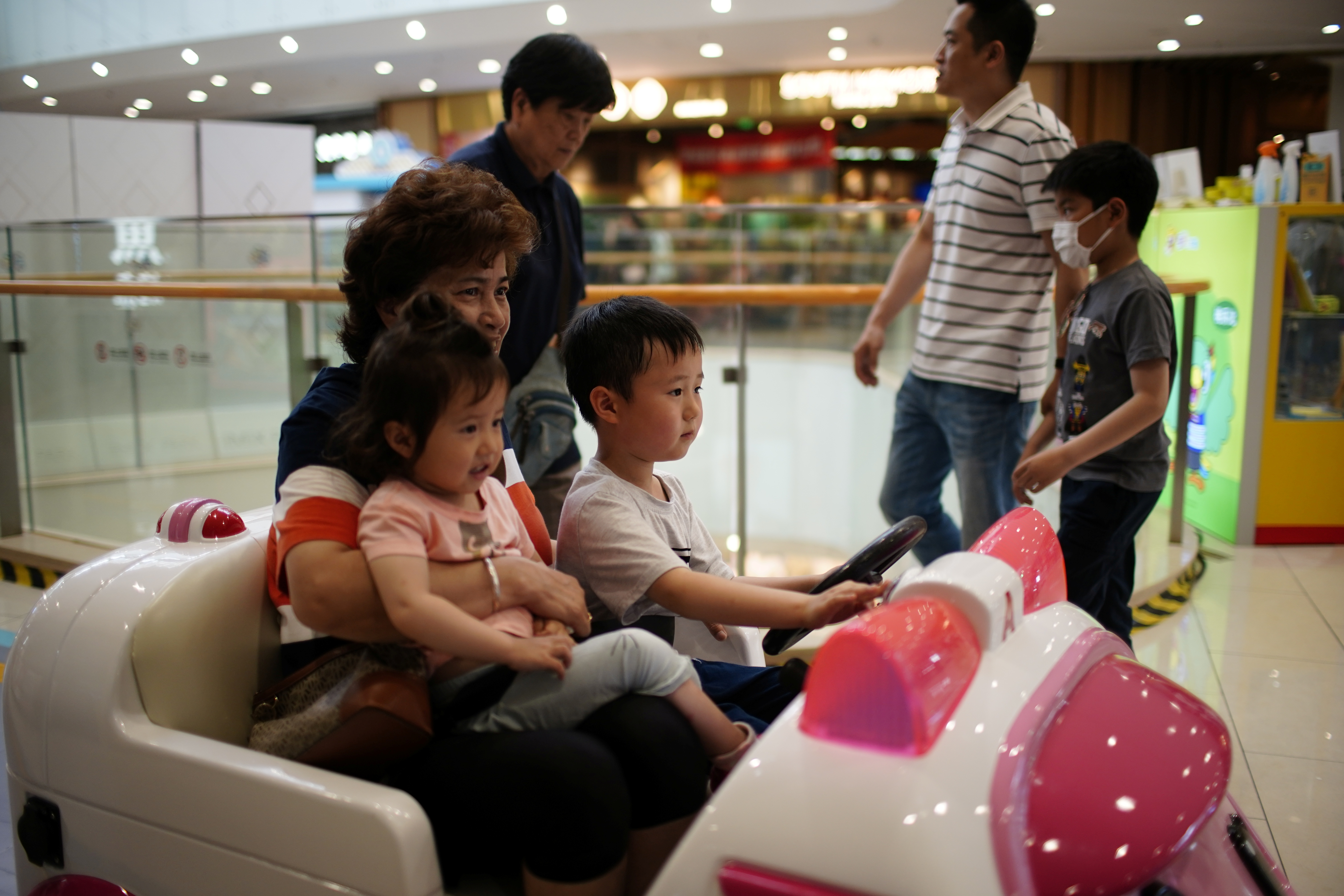 Person holds a girl as a boy drives a toy car at a shopping mall in Shanghai