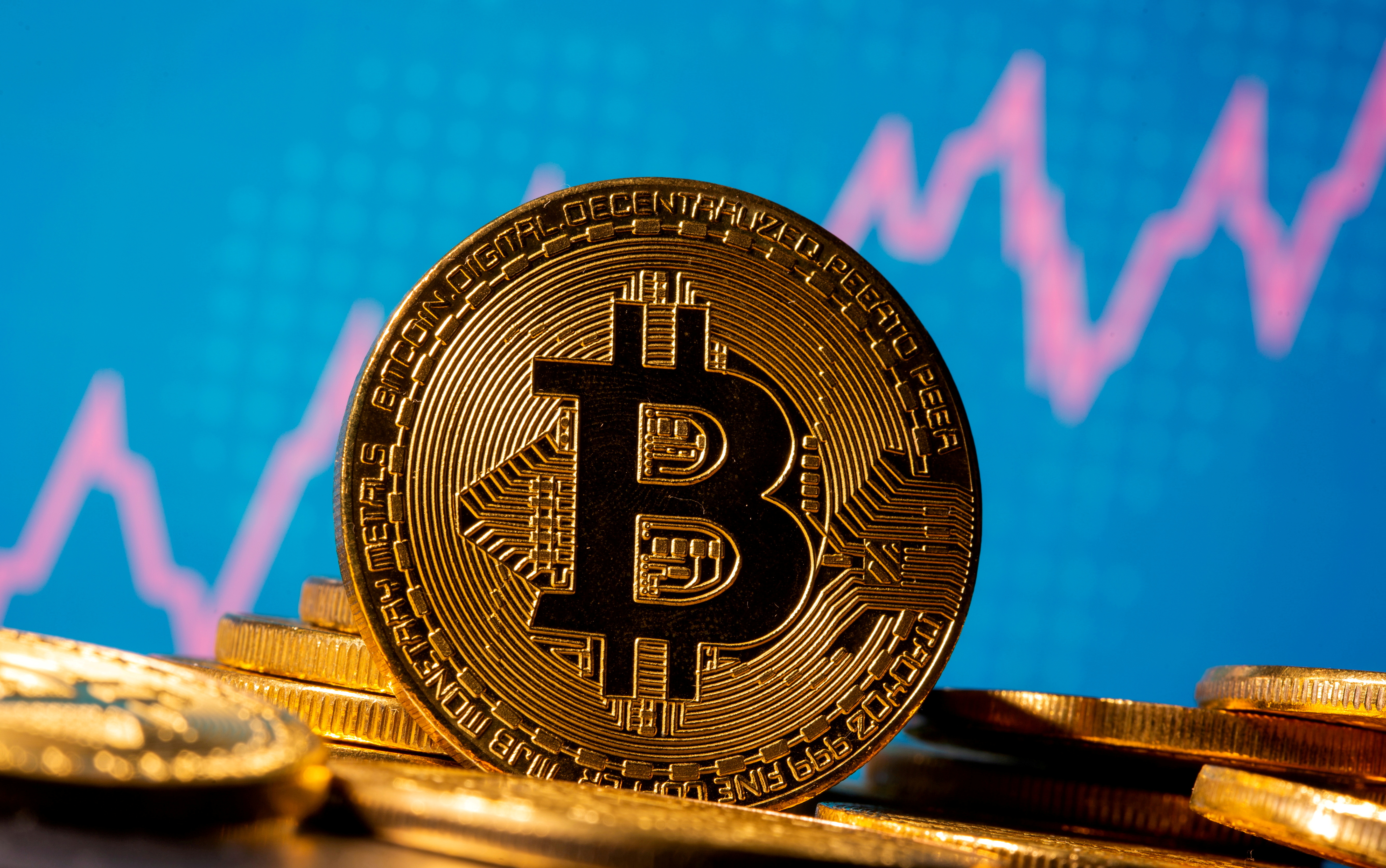 A representation of virtual currency bitcoin is seen in front of a stock graph