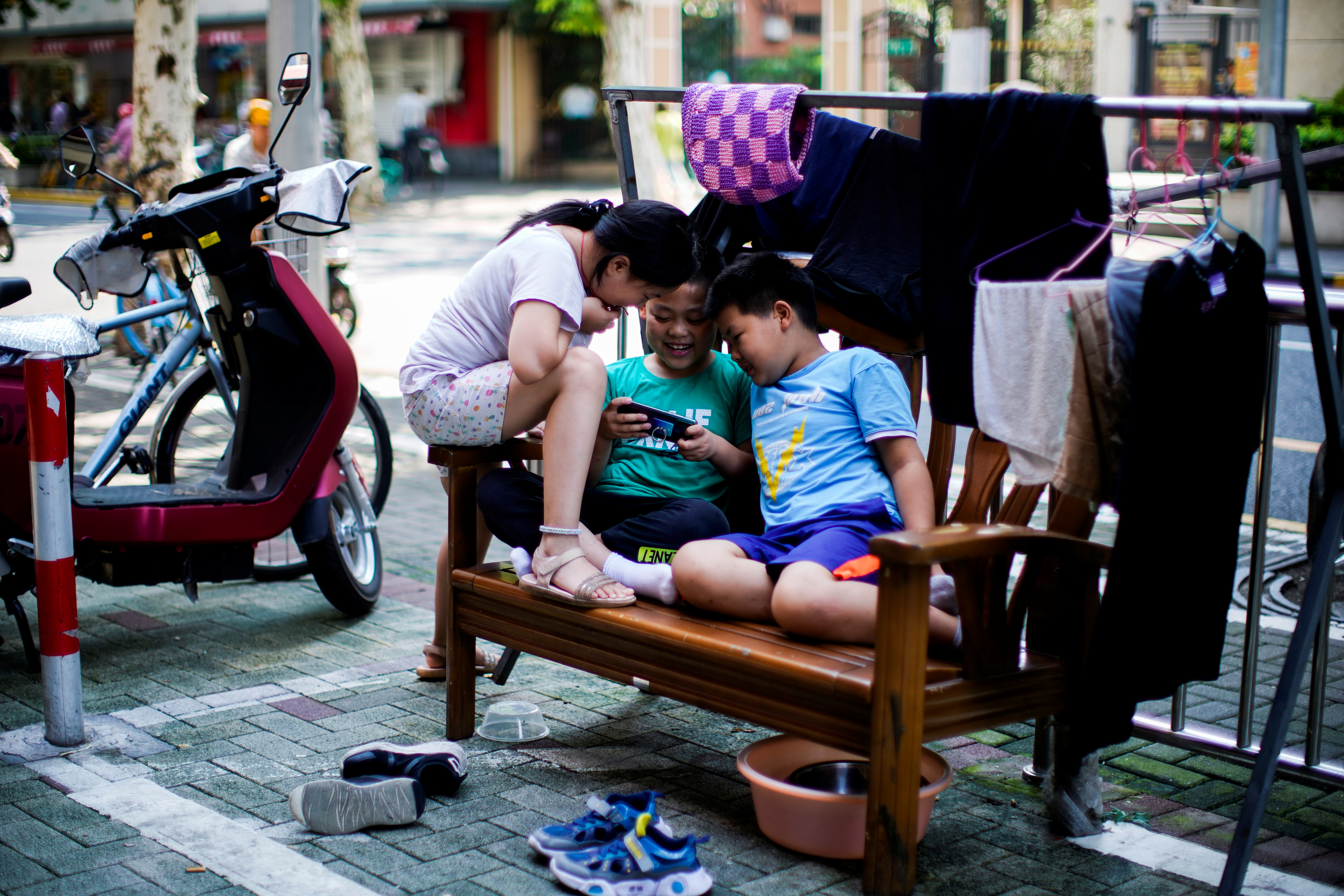 Children look at a phone on a street in Shanghai, China August 28, 2021. REUTERS/Aly Song