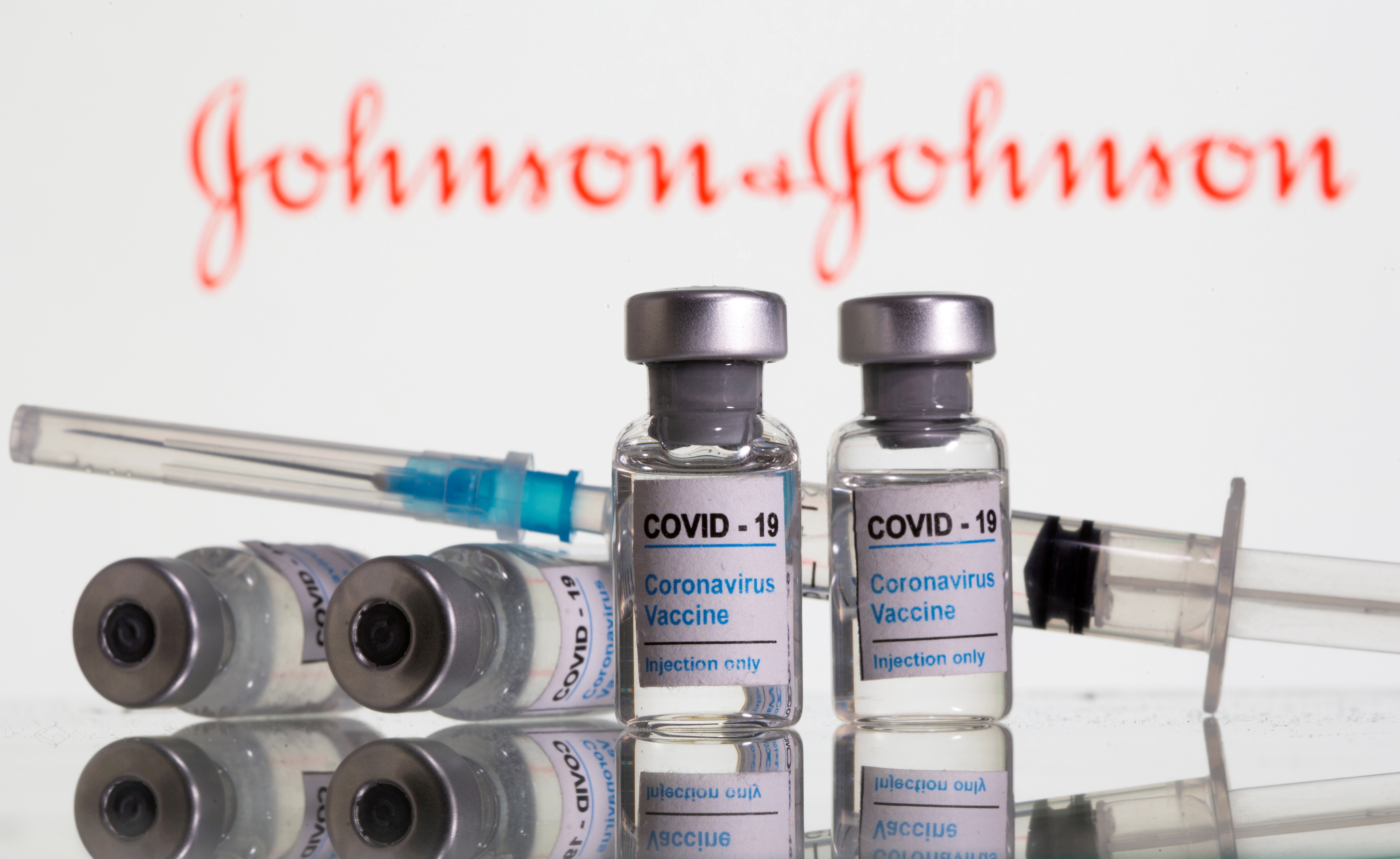 Vials labelled "COVID-19 Coronavirus Vaccine" and sryinge are seen in front of displayed J&J logo in this illustration