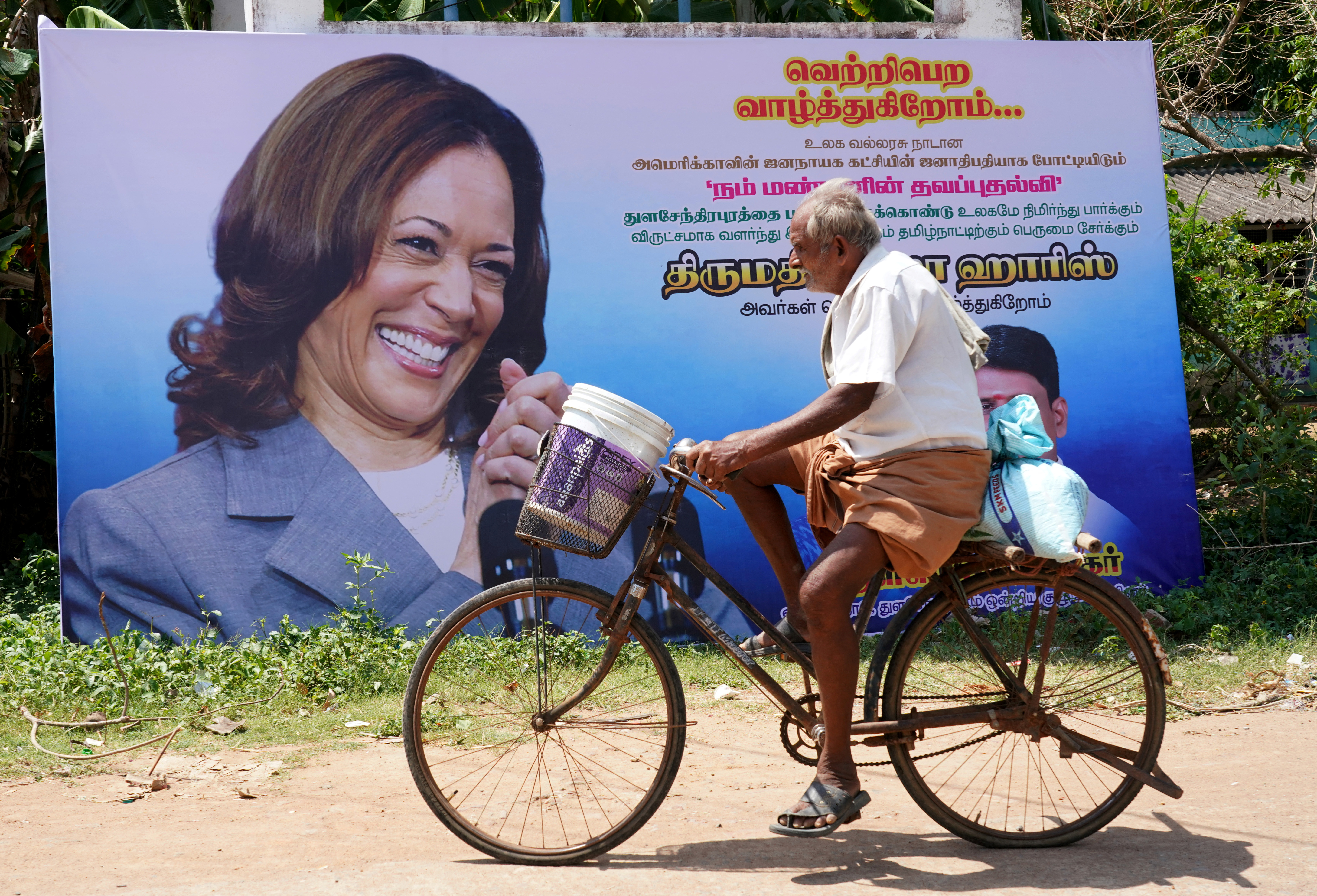 A man rides his bicycle past a banner of U.S. Vice President Harris installed alongside a road in the village of Thulasendrapuram