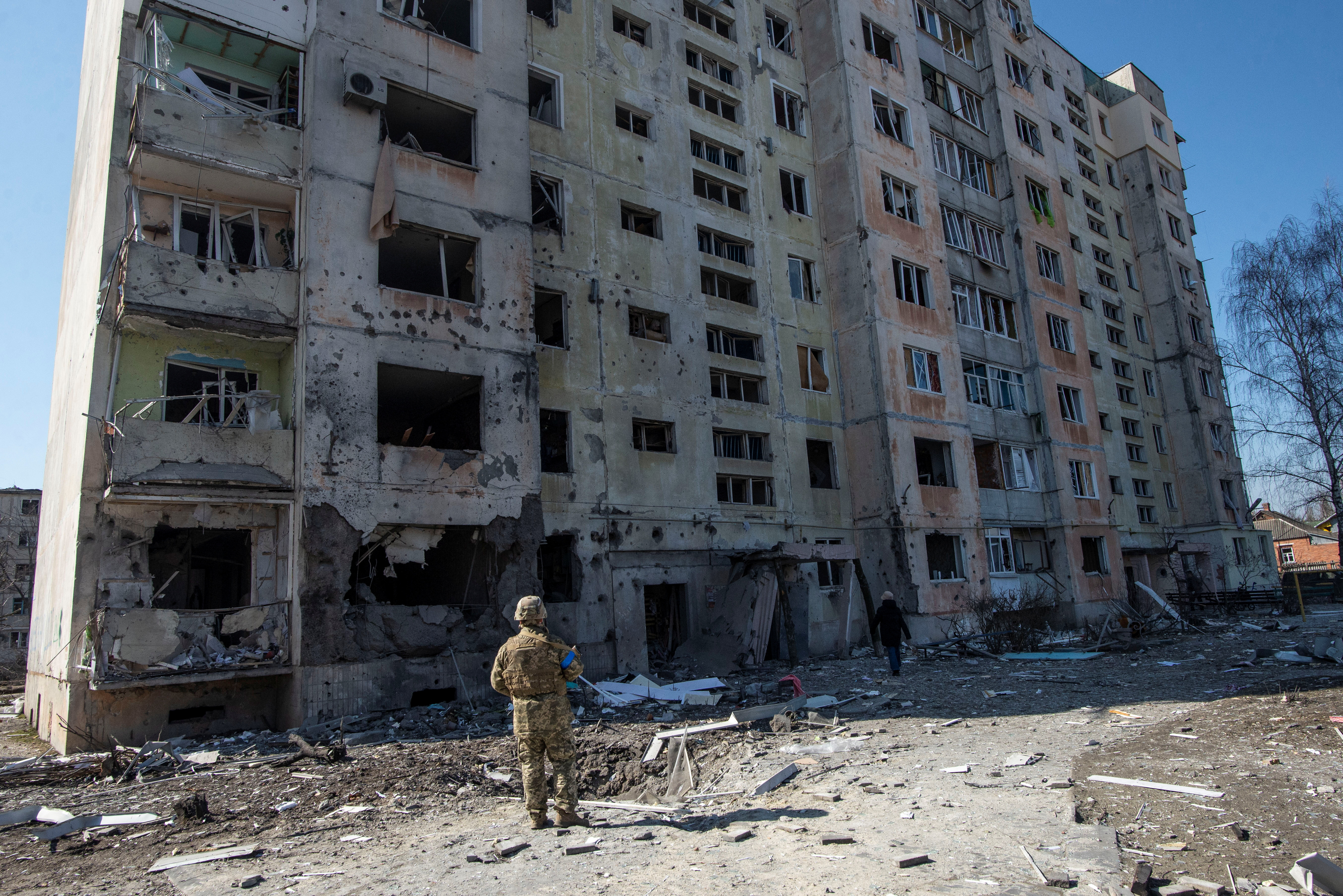 A Ukrainian service member stands in a front of a residential building damaged by a shelling in the town of Okhtyrka