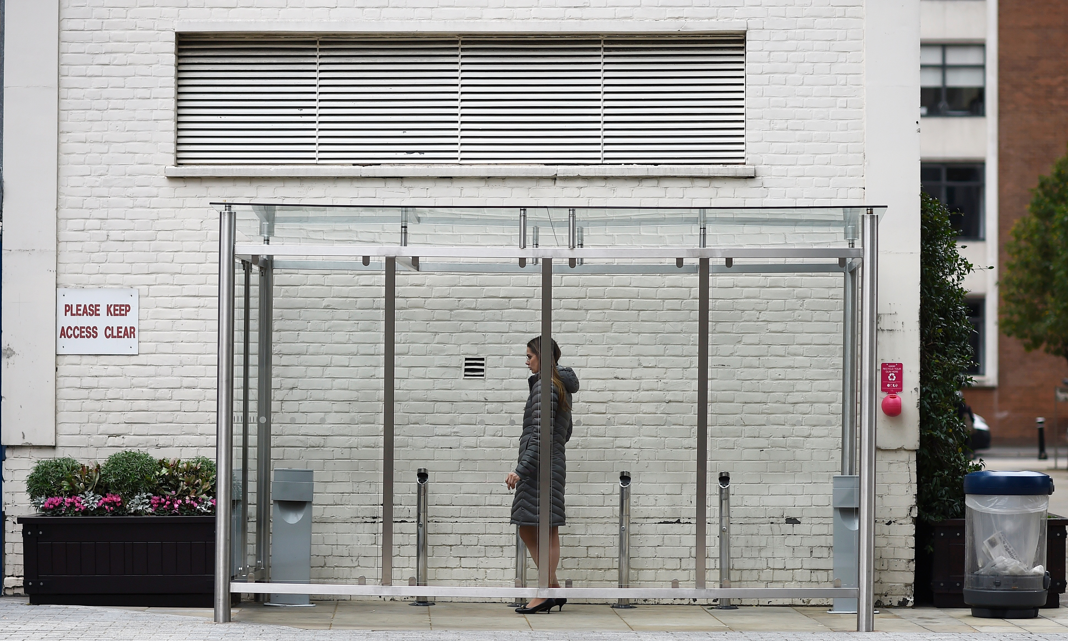 A woman smokes a cigarette in glass shelter for smokers in the City of London