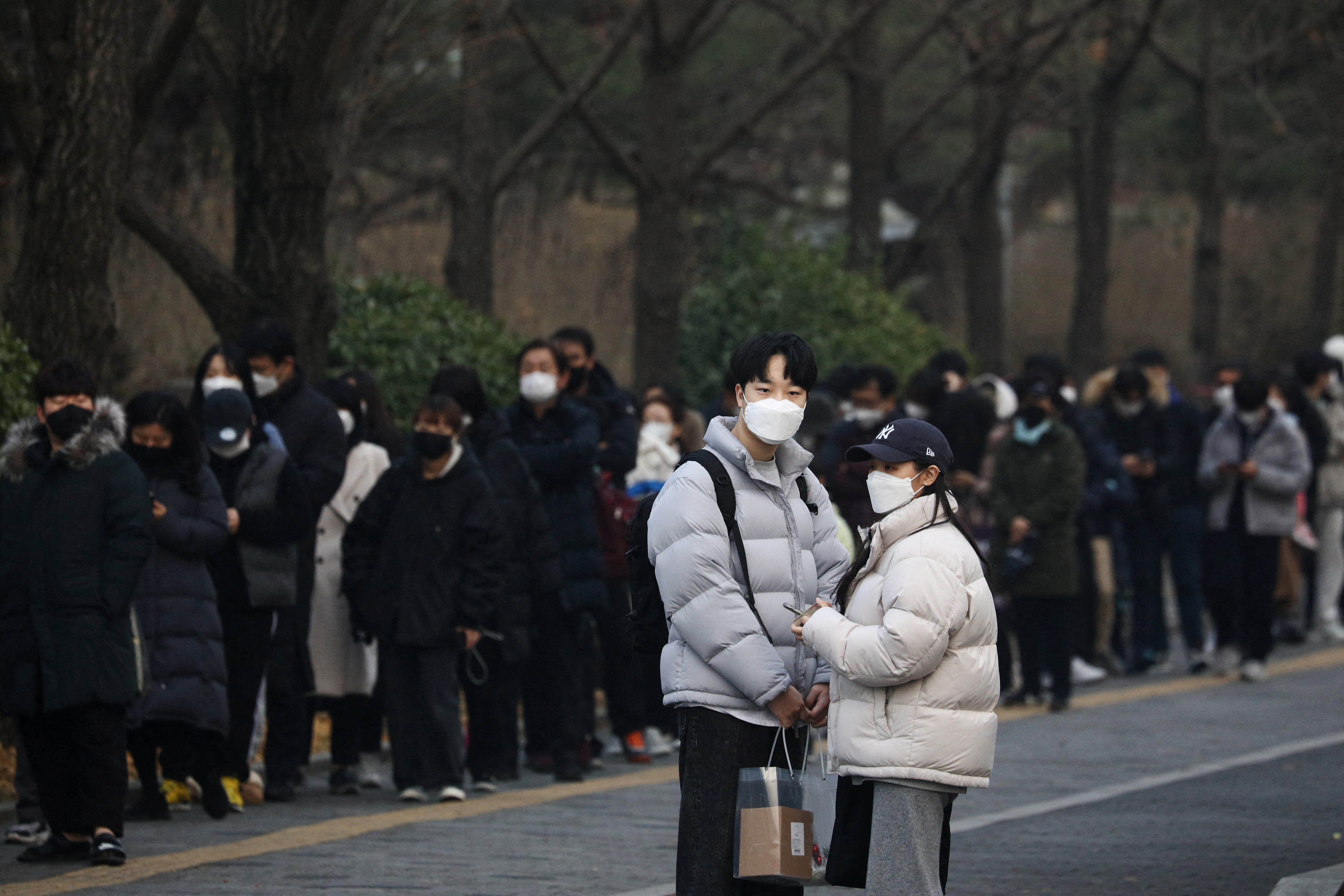 A couple stands next to people waiting in a long line to undergo coronavirus disease (COVID-19) test at a testing site in Seoul
