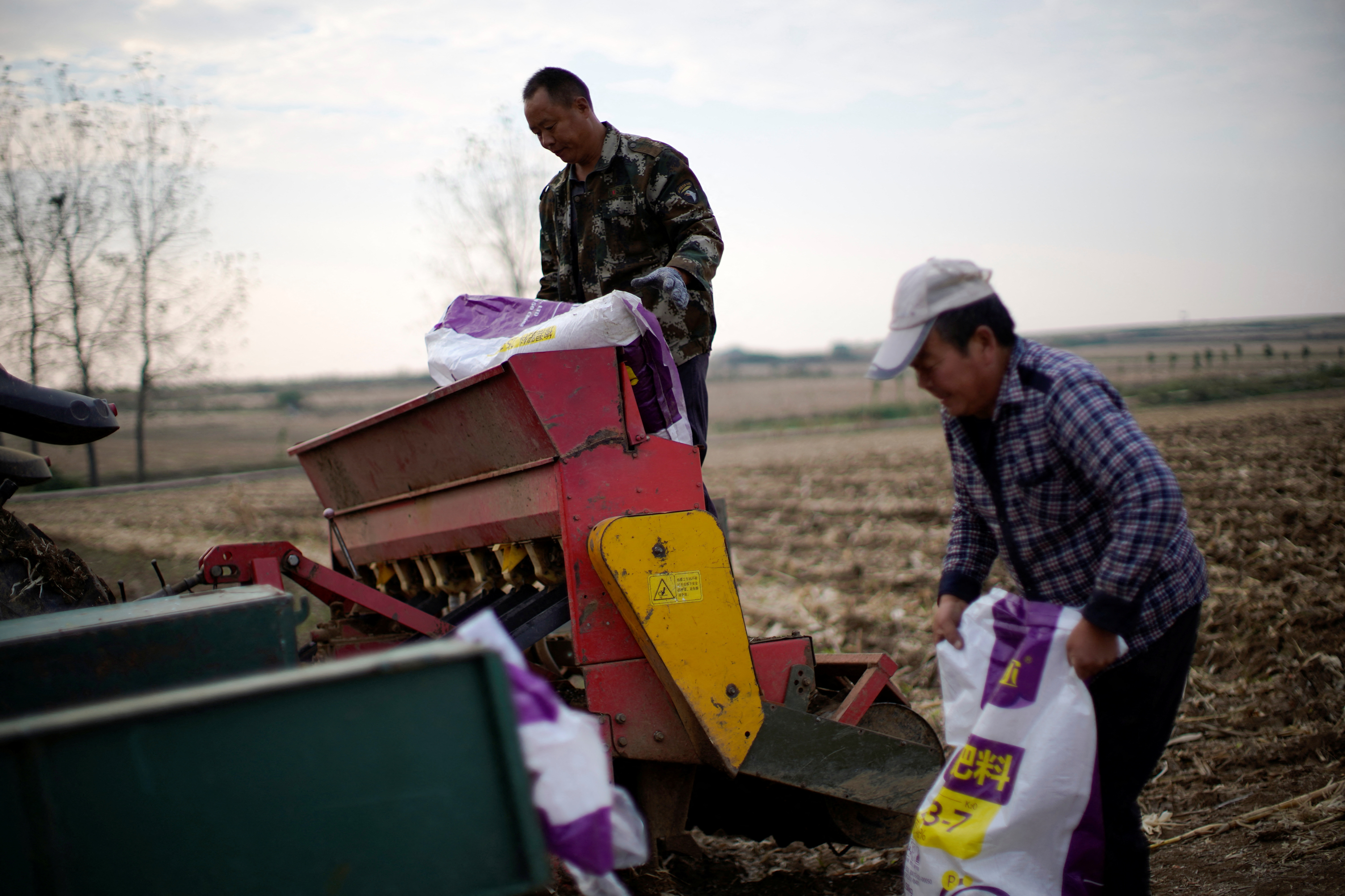 Farmers load sacks of fertiliser into a seeder on a wheat field in Nanyang