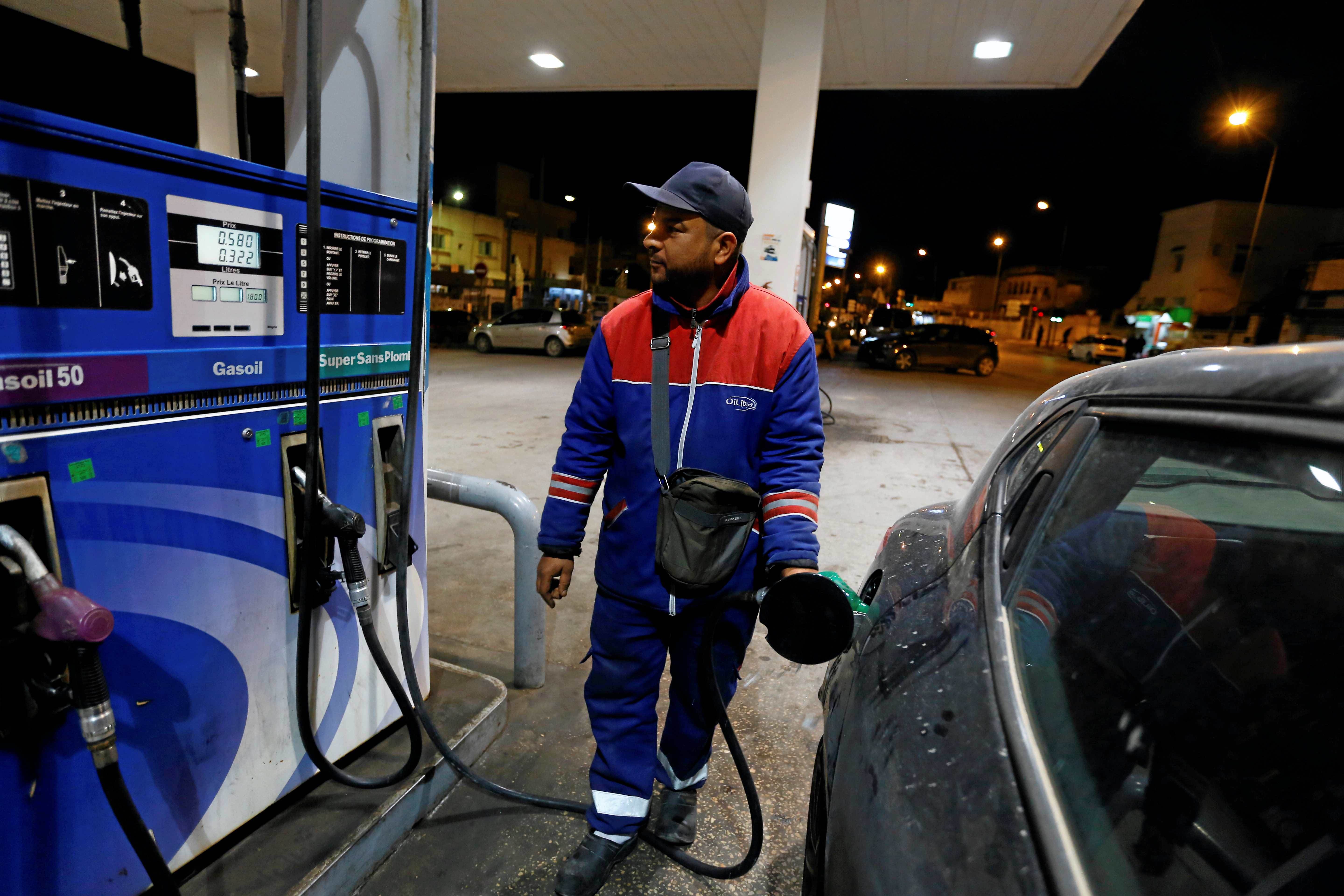 A gas station attendant pumps fuel into a customer's car at a gas station in Tunis