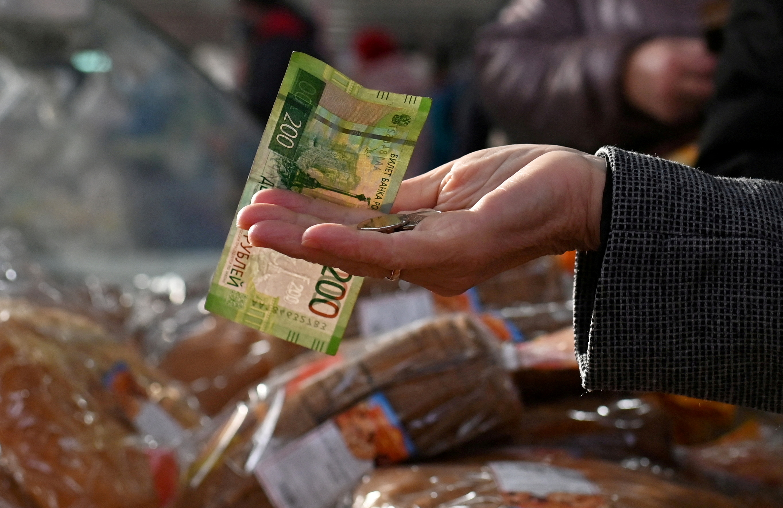 A customer hands over Russian rouble banknotes and coins to a vendor at a market in Omsk
