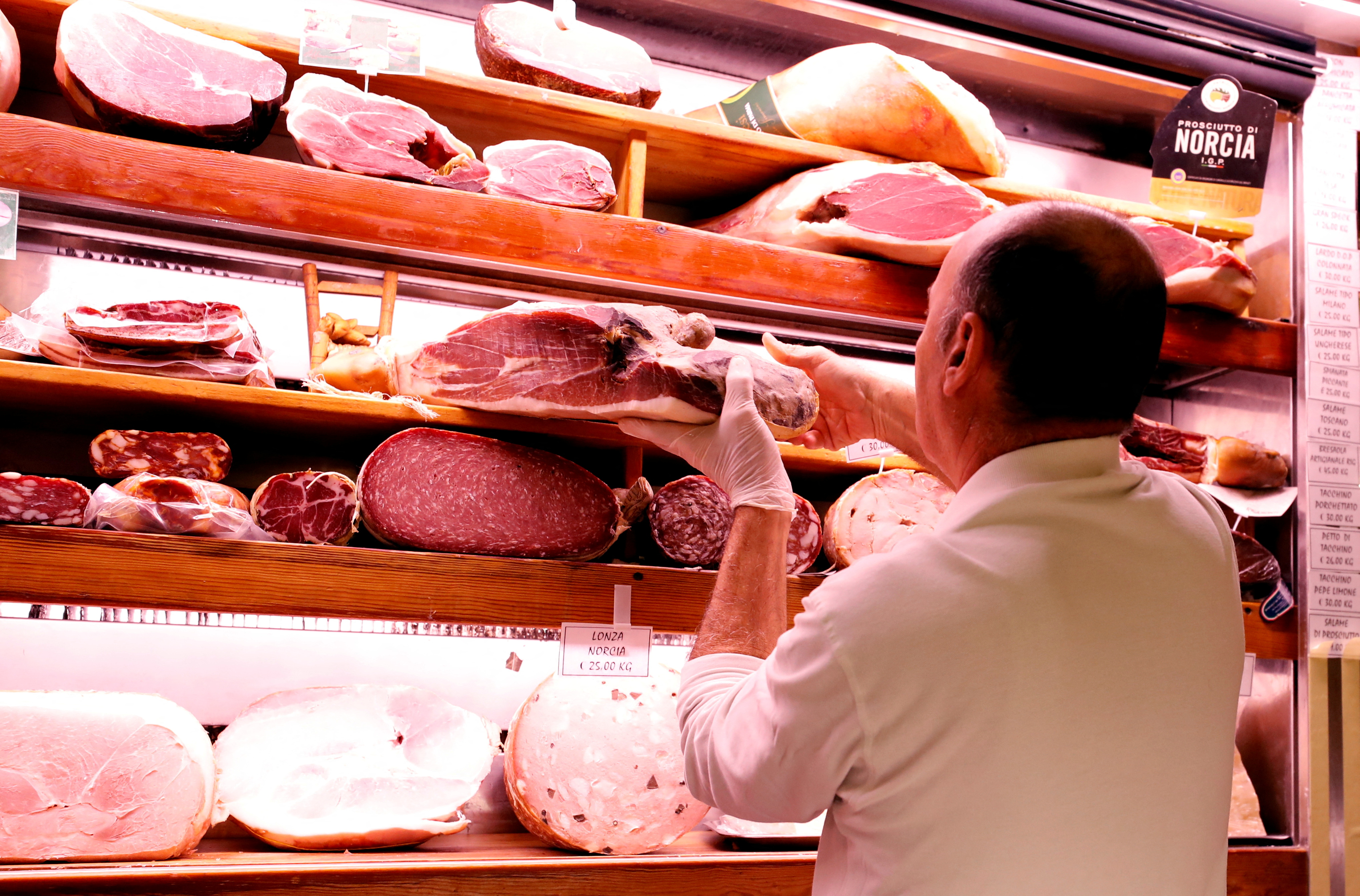 A grocer holds a piece of prosciutto ham in a deli in Rome