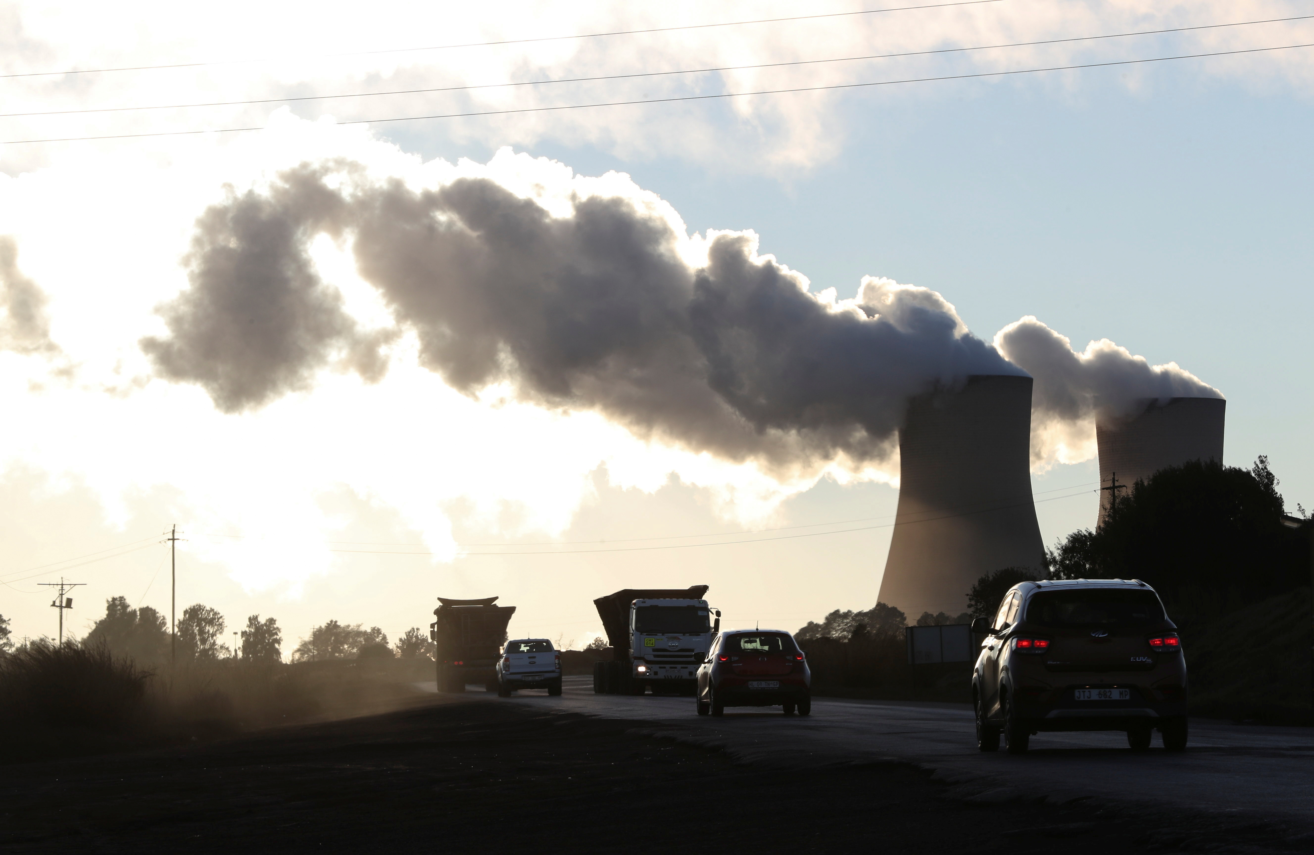 Trucks and cars are seen driving past while smoke rises from the Duvha coal-based power station owned by state power utility Eskom in Emalahleni