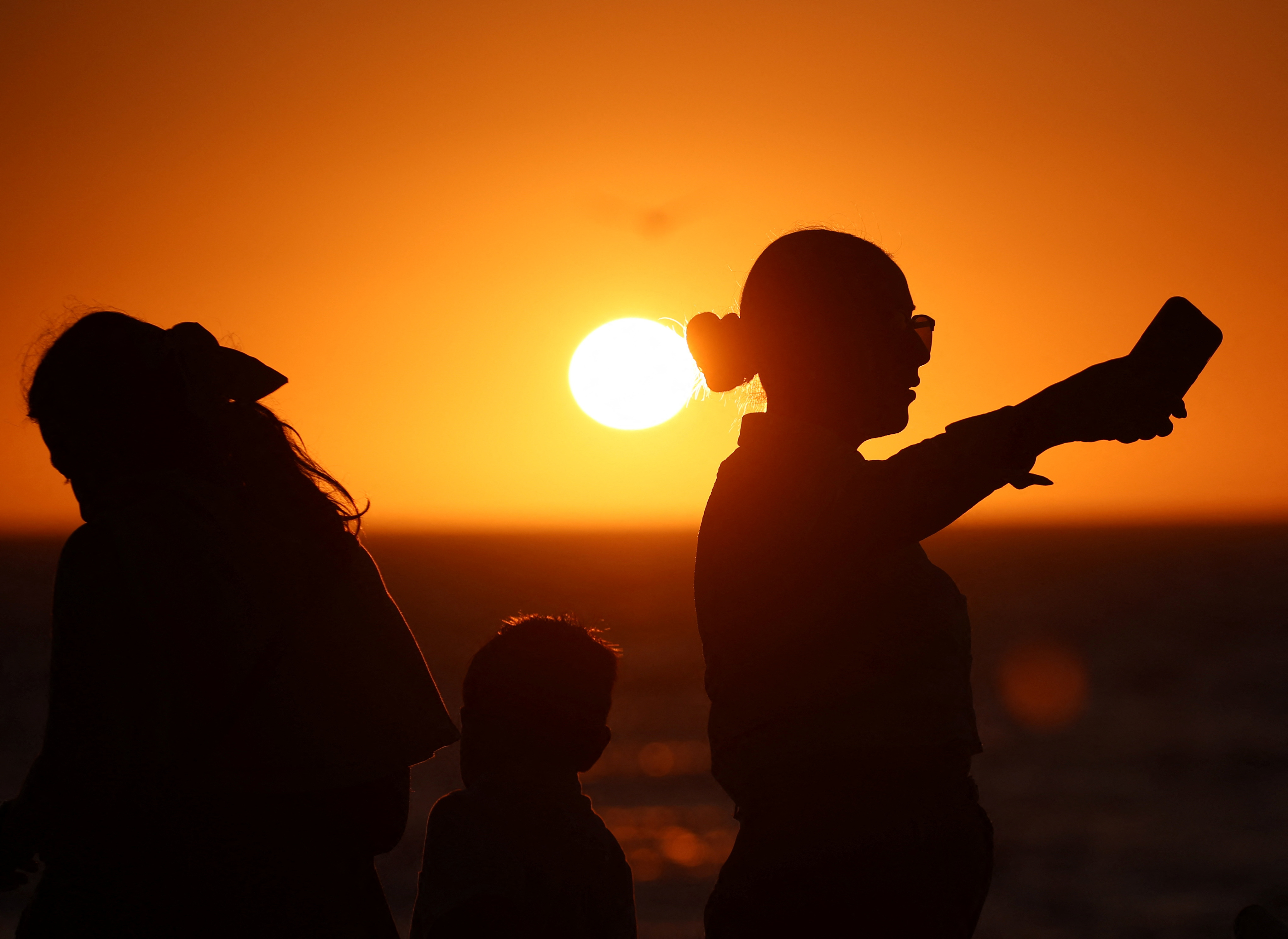 People are silhouetted at sunset as they visit the Malecon, one day ahead of a total solar eclipse, in Mazatlan