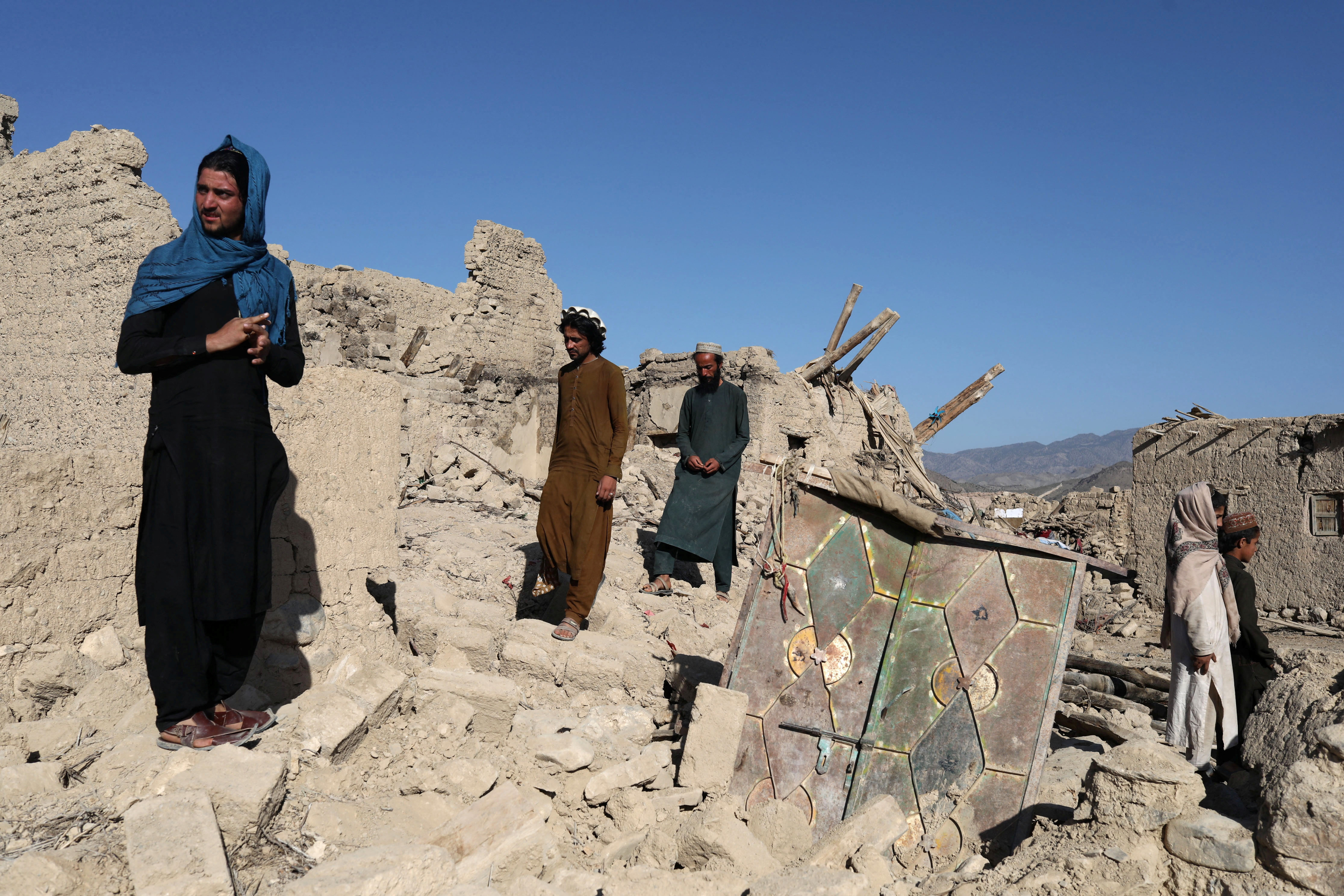 Afghan men stand on the debris of damaged houses after the recent eartquacke in Wor Kali village
