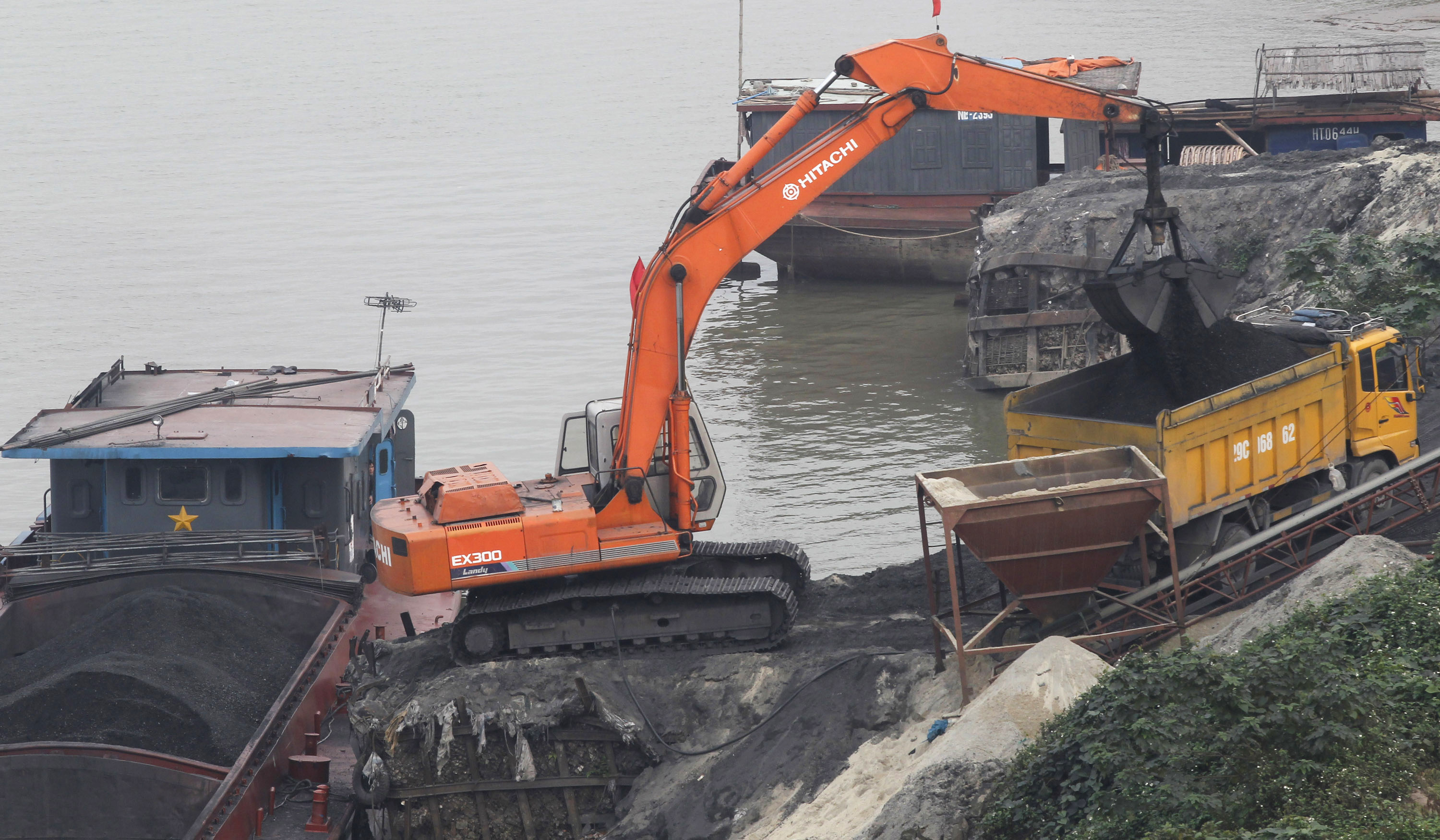 An excavator transfers coal from a ship onto a truck at a coal port in Hanoi