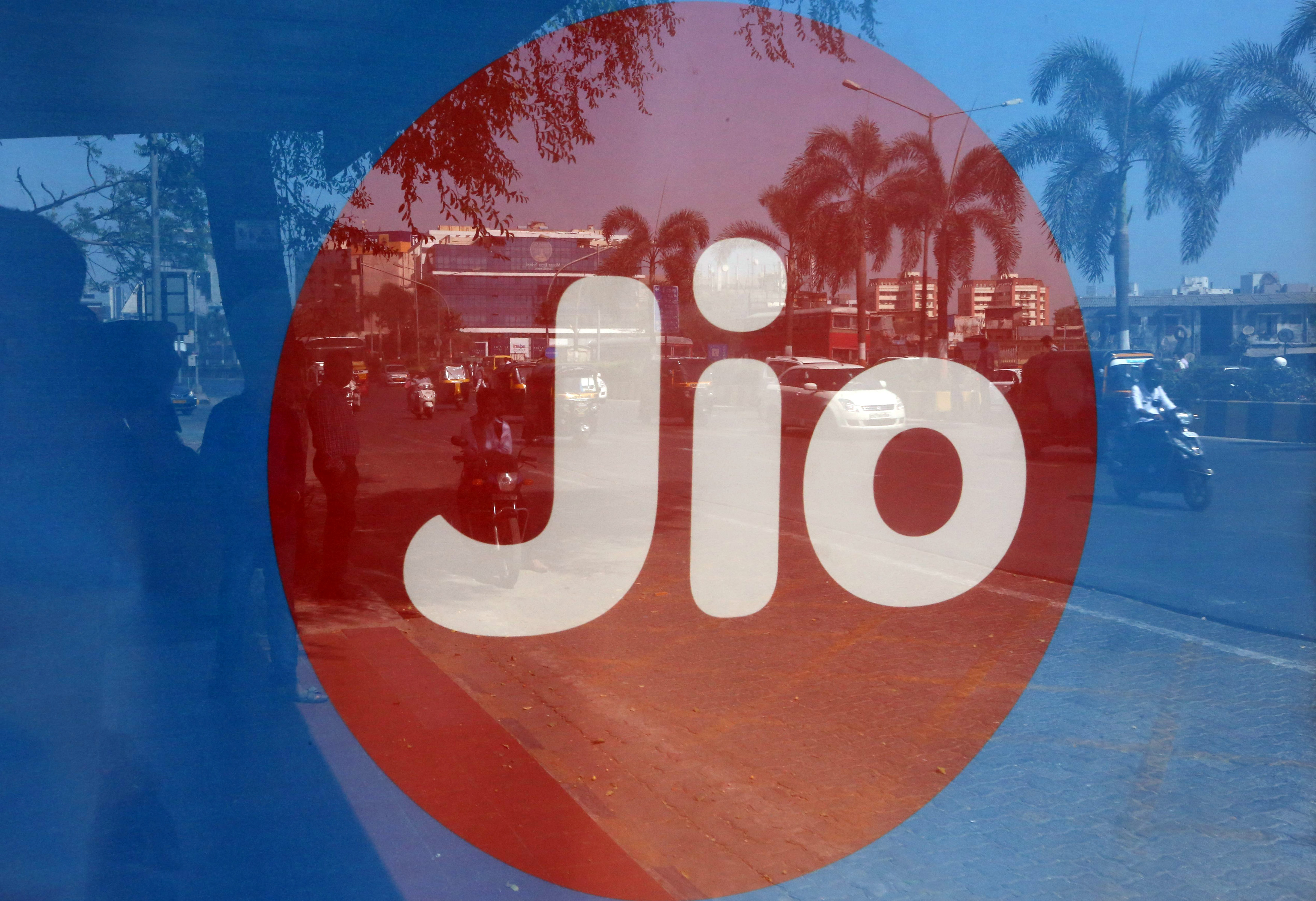 Commuters are reflected on an advertisement of Reliance Industries' Jio telecoms unit, at a bus stop in Mumbai