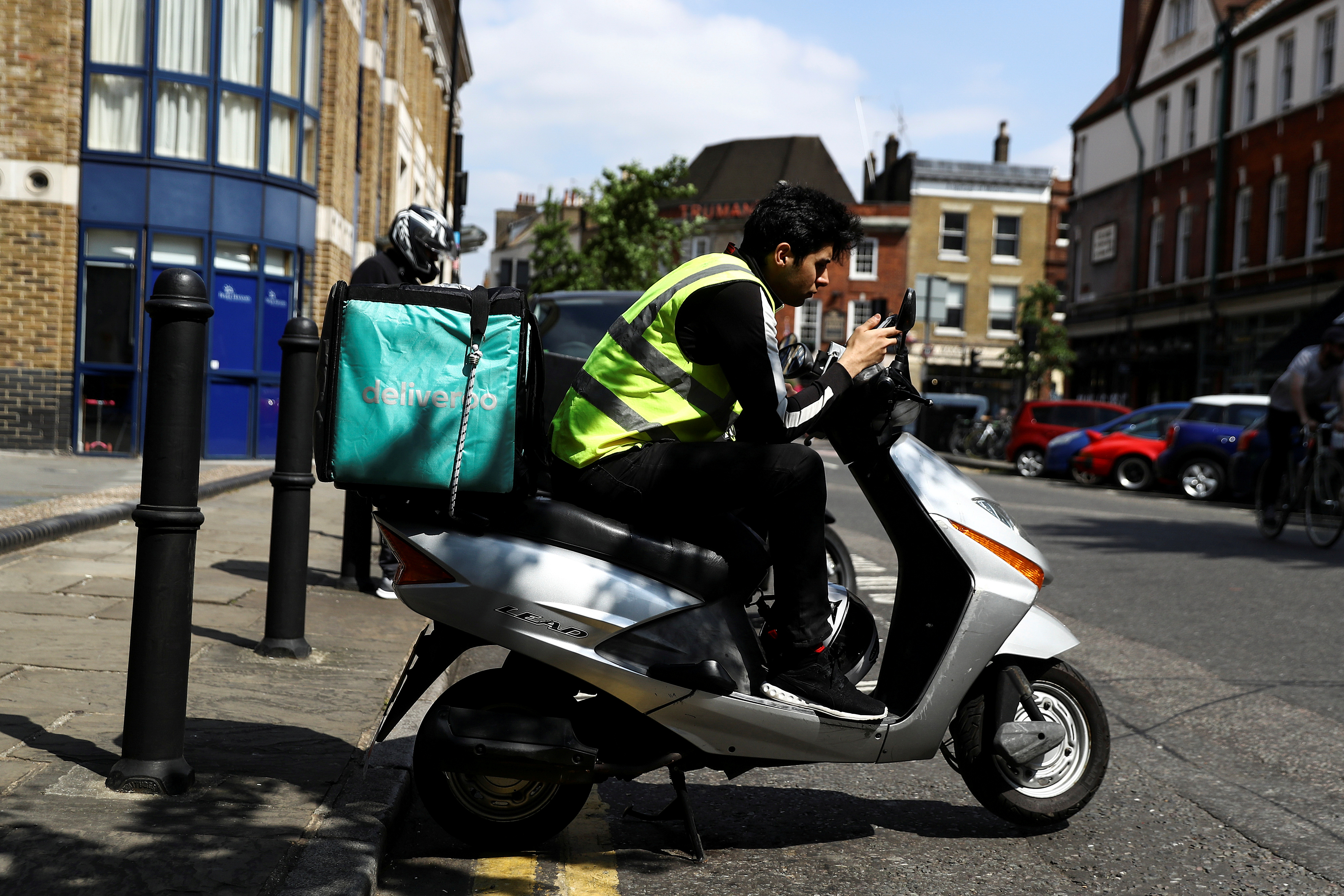 A Deliveroo scooter driver takes a break between deliveries in London