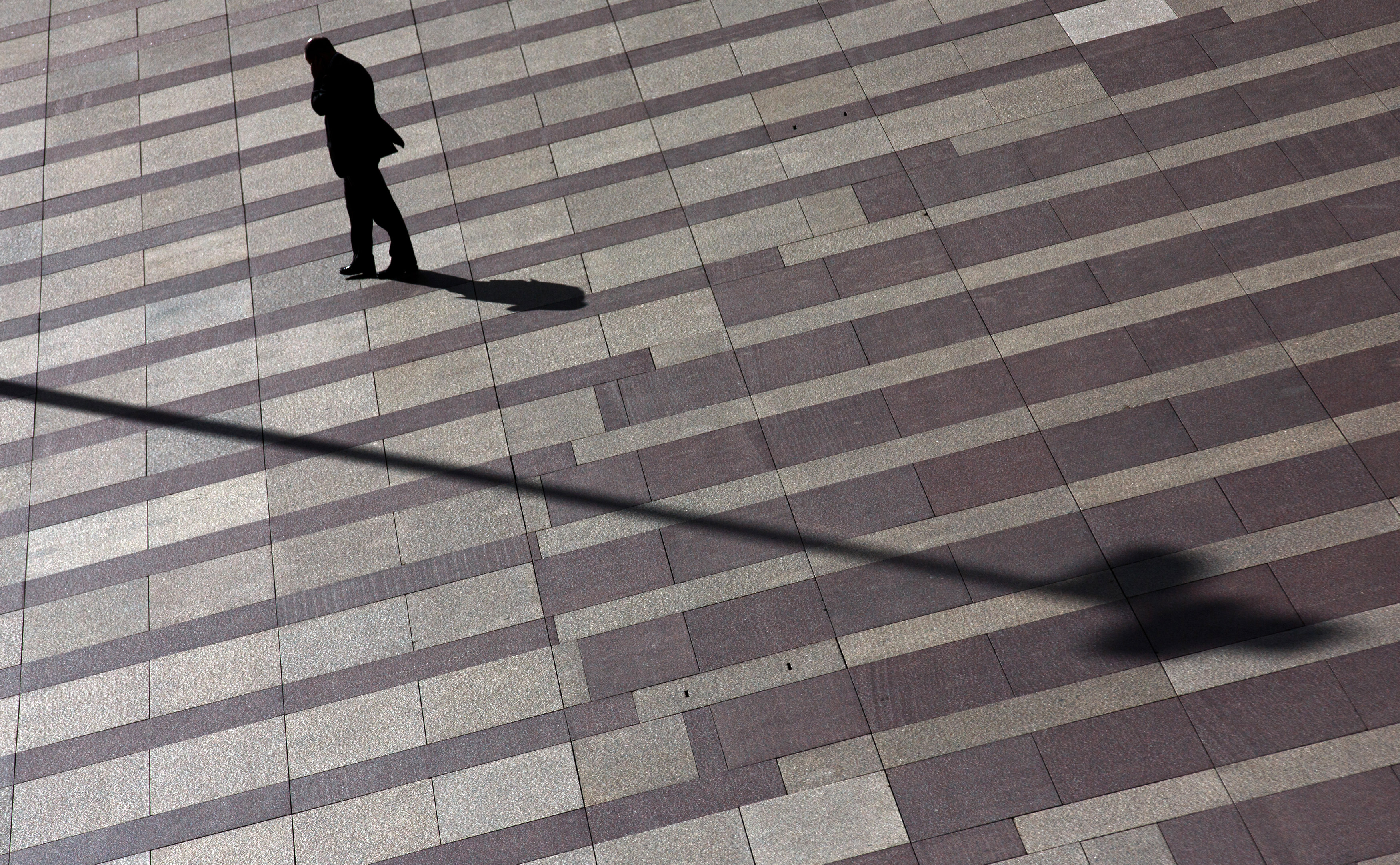 Man talks on mobile phone as he walks on a patterned floor at a yard outside an office building in Madrid's financial district