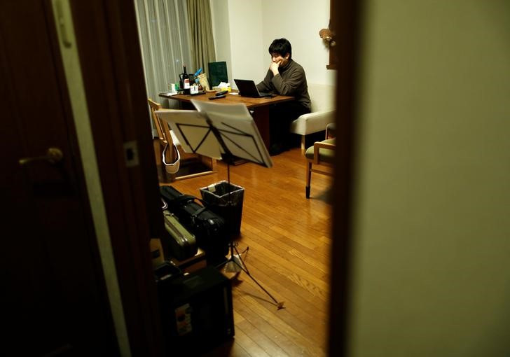 Seijiro Katsura, an office worker, checks market rates for investment opportunities using his laptop at his home in Tokyo, Japan