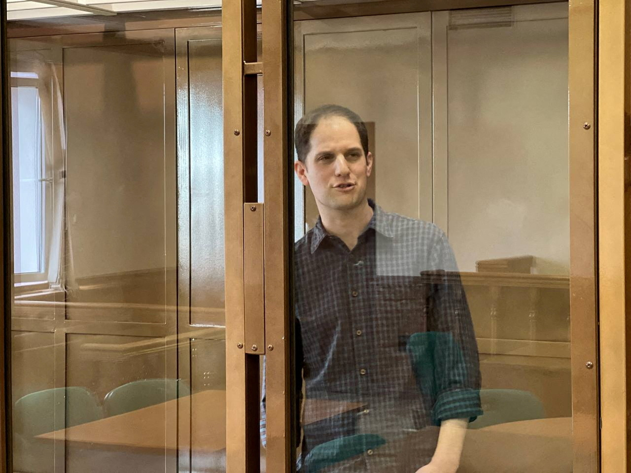 Wall Street Journal reporter Evan Gershkovich stands behind a glass wall of an enclosure for defendants as he attends a court hearing to consider extending his detention in Moscow