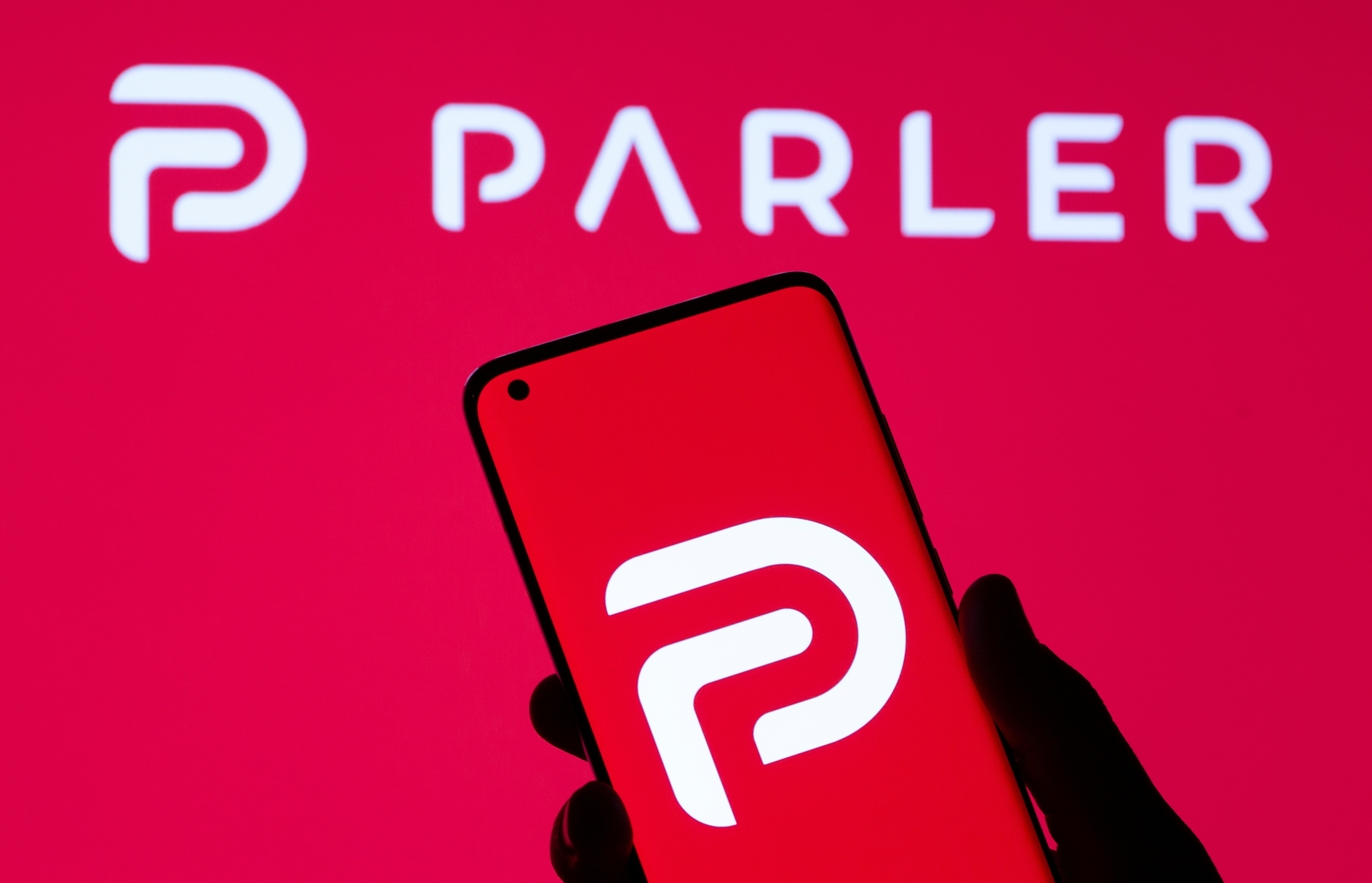 Woman holding smartphone with Parler logo in front of displayed same logo in this illustration