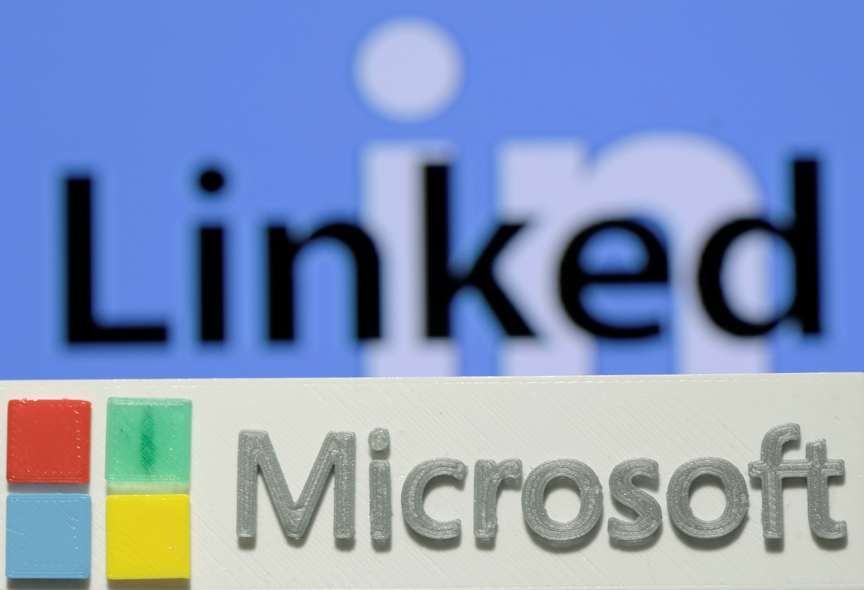 A 3D printed logo of Microsoft is seen in front of a displayed LinkedIn logo in this illustration