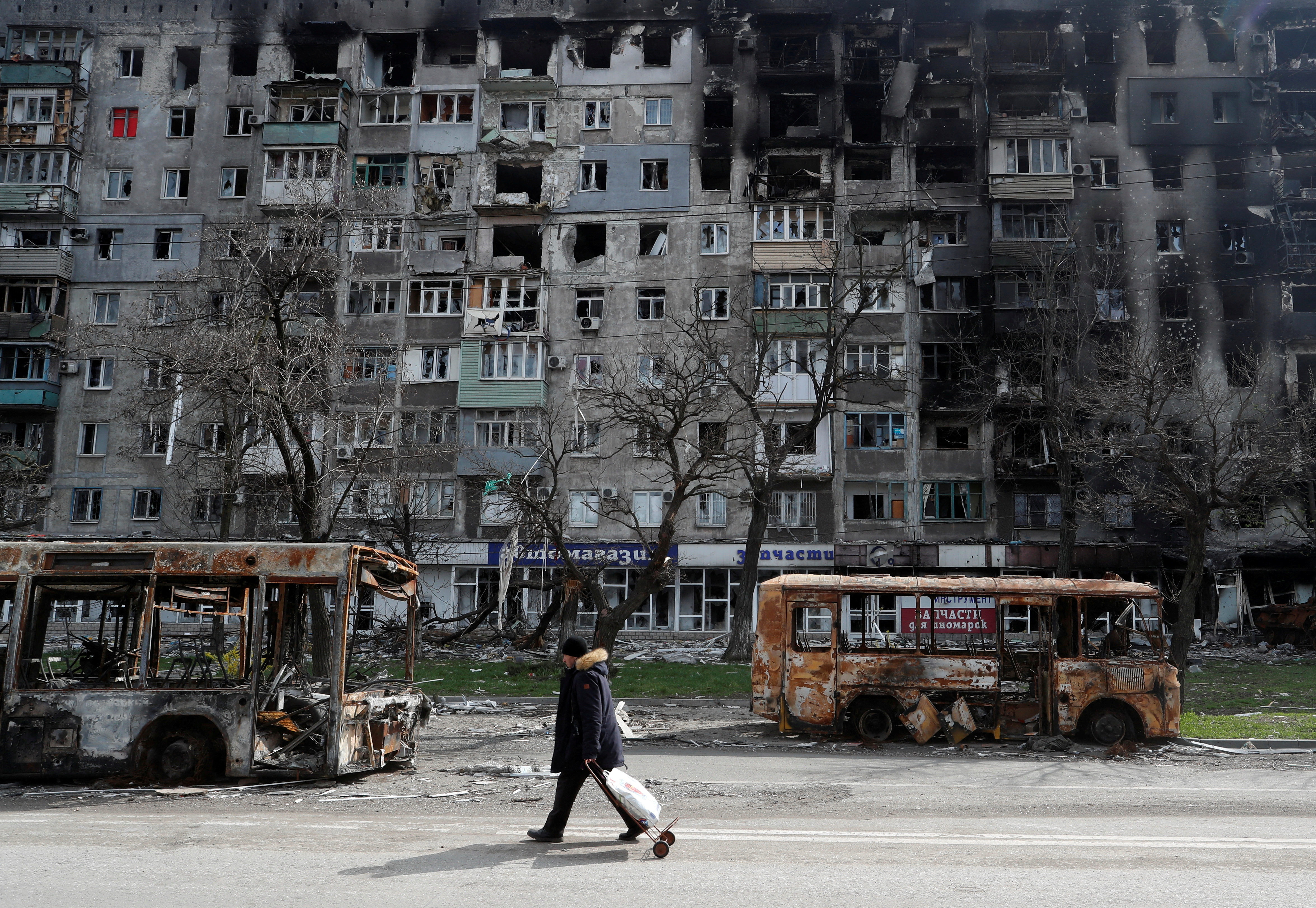 A local resident walks along a street past burnt out buses in Mariupol