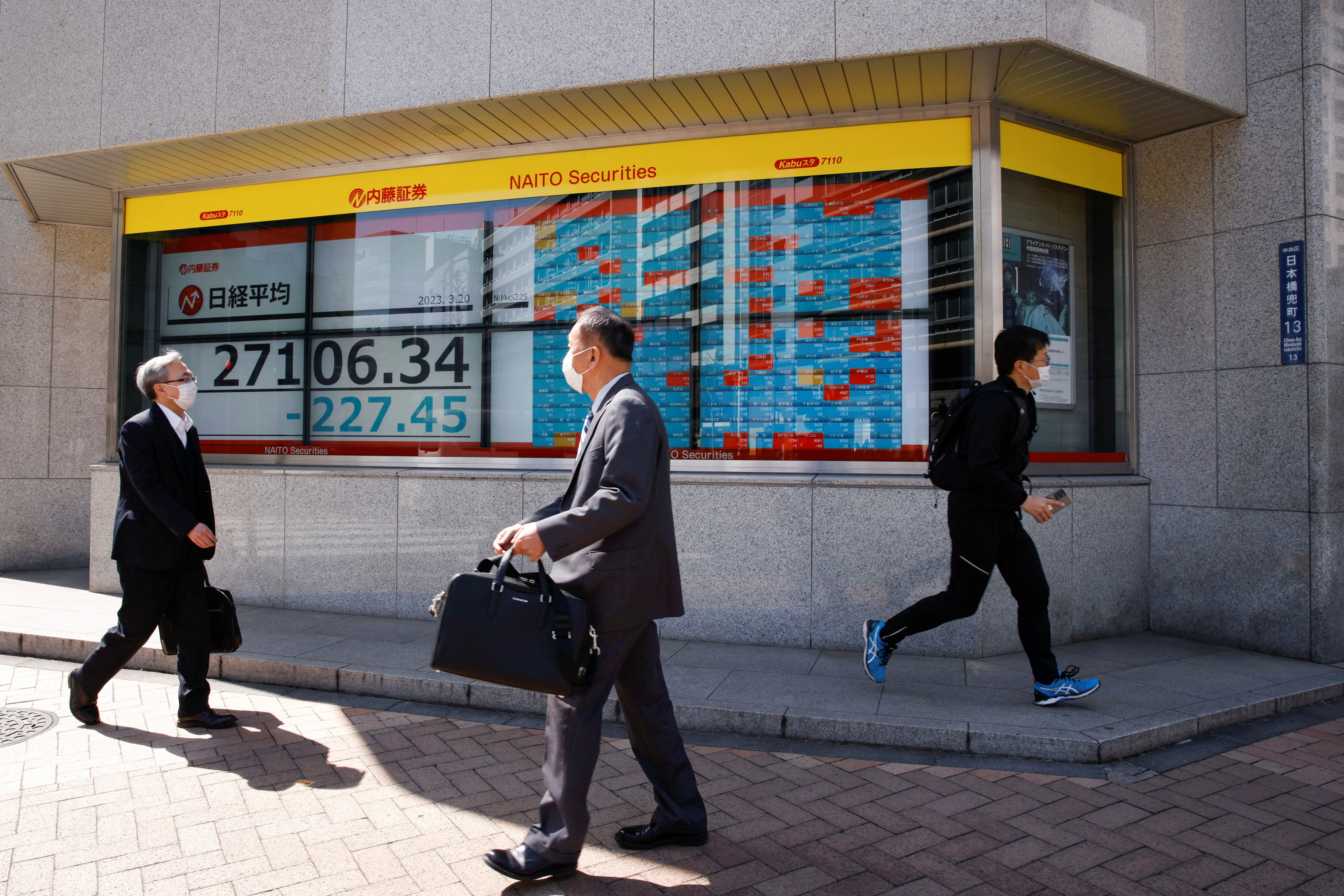 Passersby walk past an electronic board showing Japan's Nikkei average and stock quotations outside a brokerage, in Tokyo