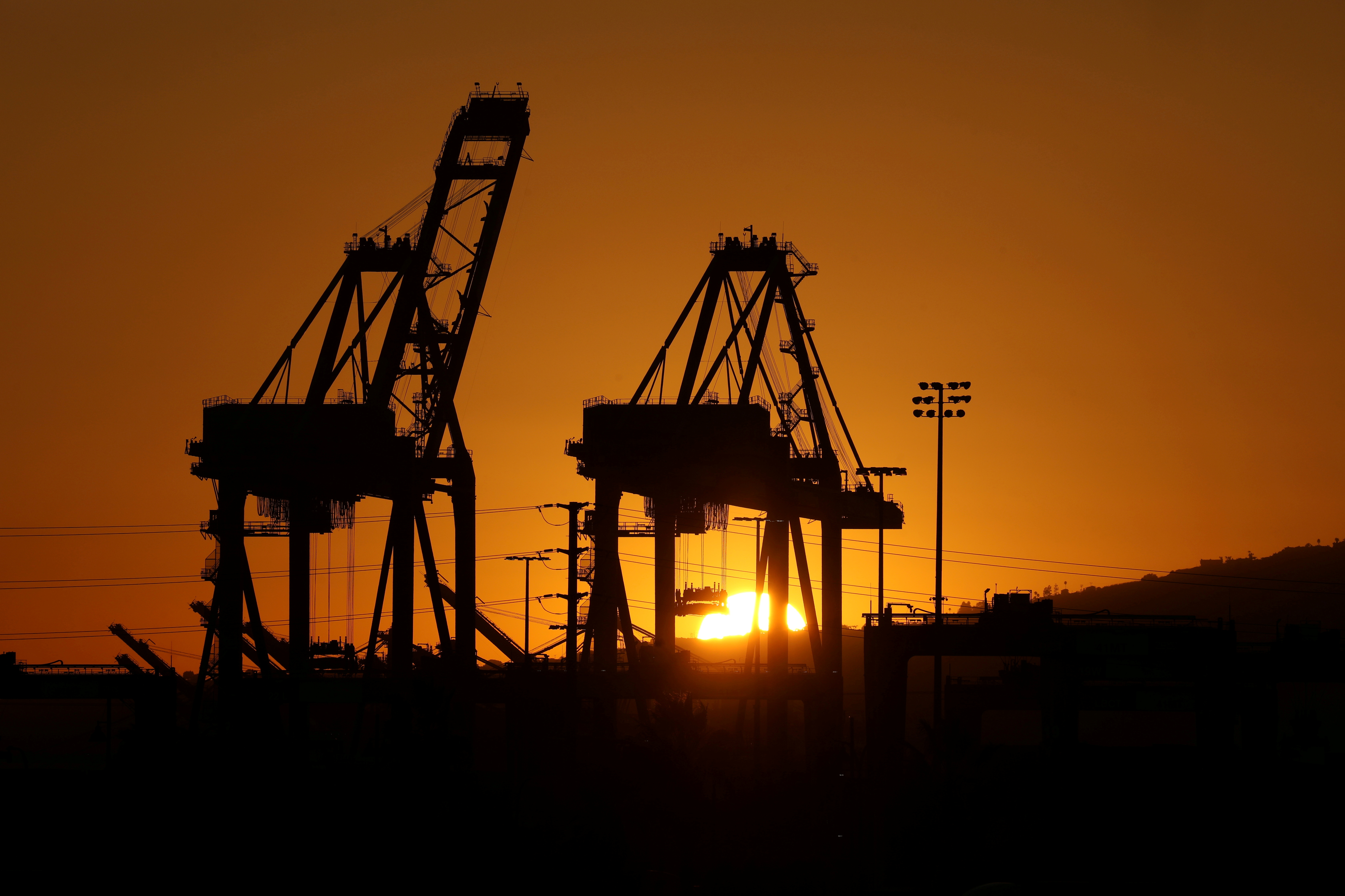 The sun sets behind container cranes at the Port of Los Angeles, California