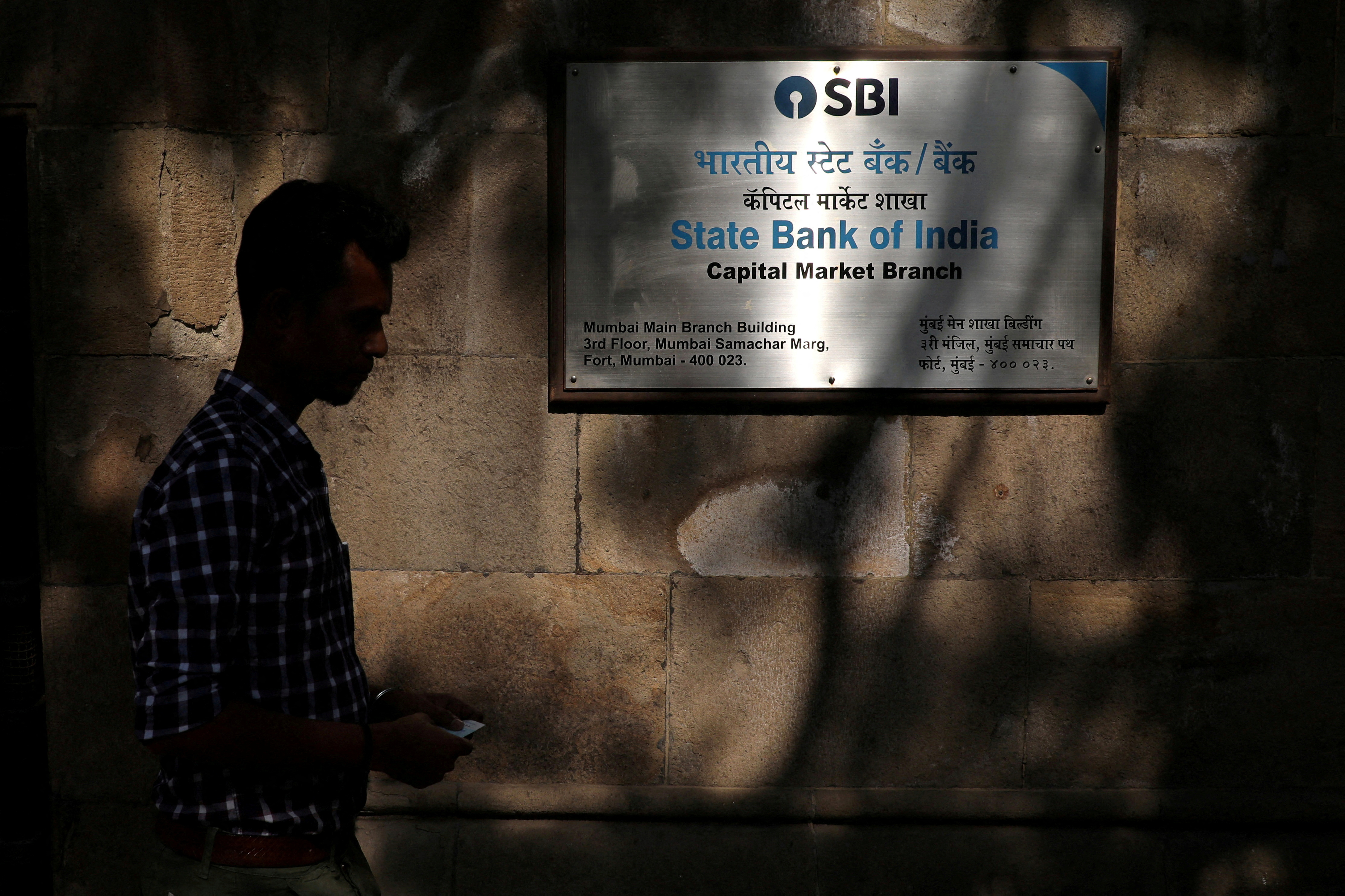 FILE PHOTO: A man walks in front of a signboard displayed at the head office of SBI in Mumbai