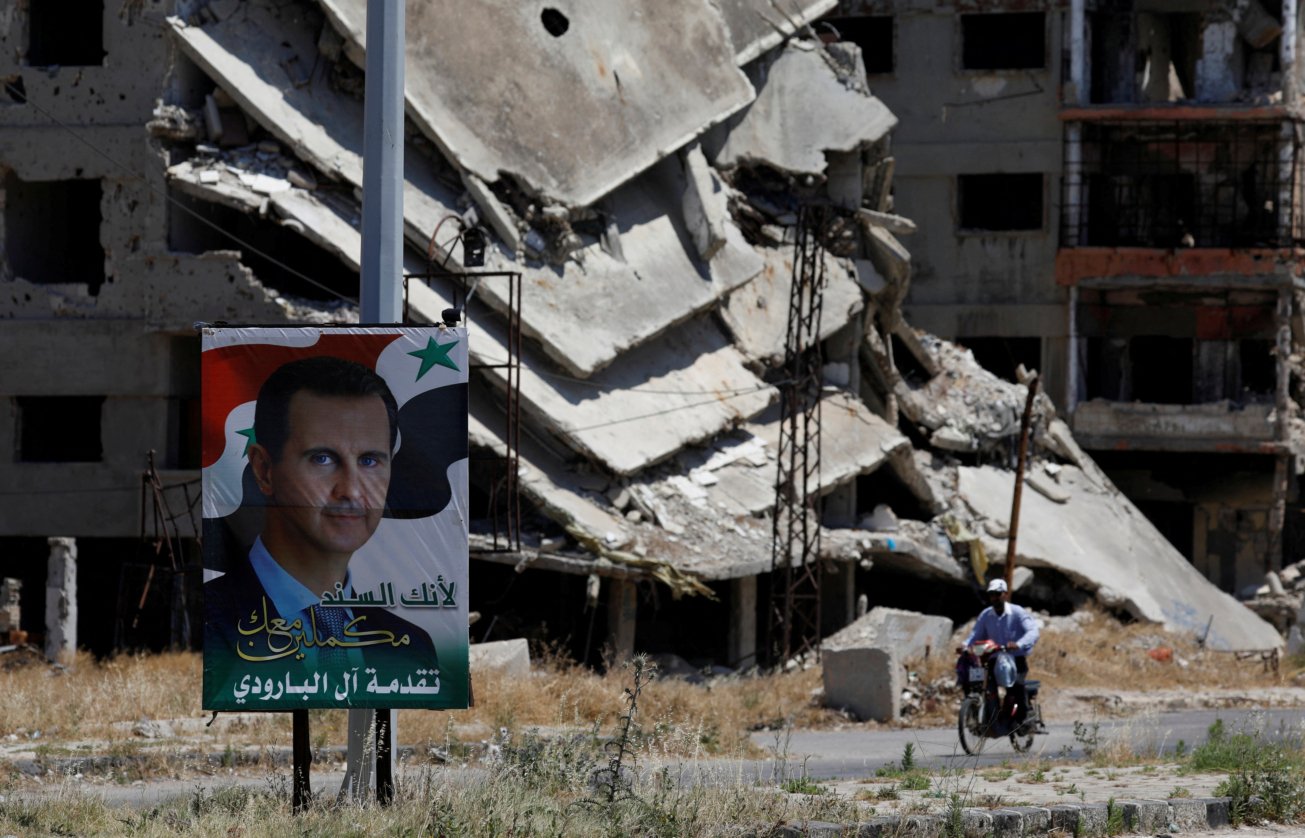 A poster depciting Syria's President Bashar al-Assad is pictured in front of damaged buildings in Homs