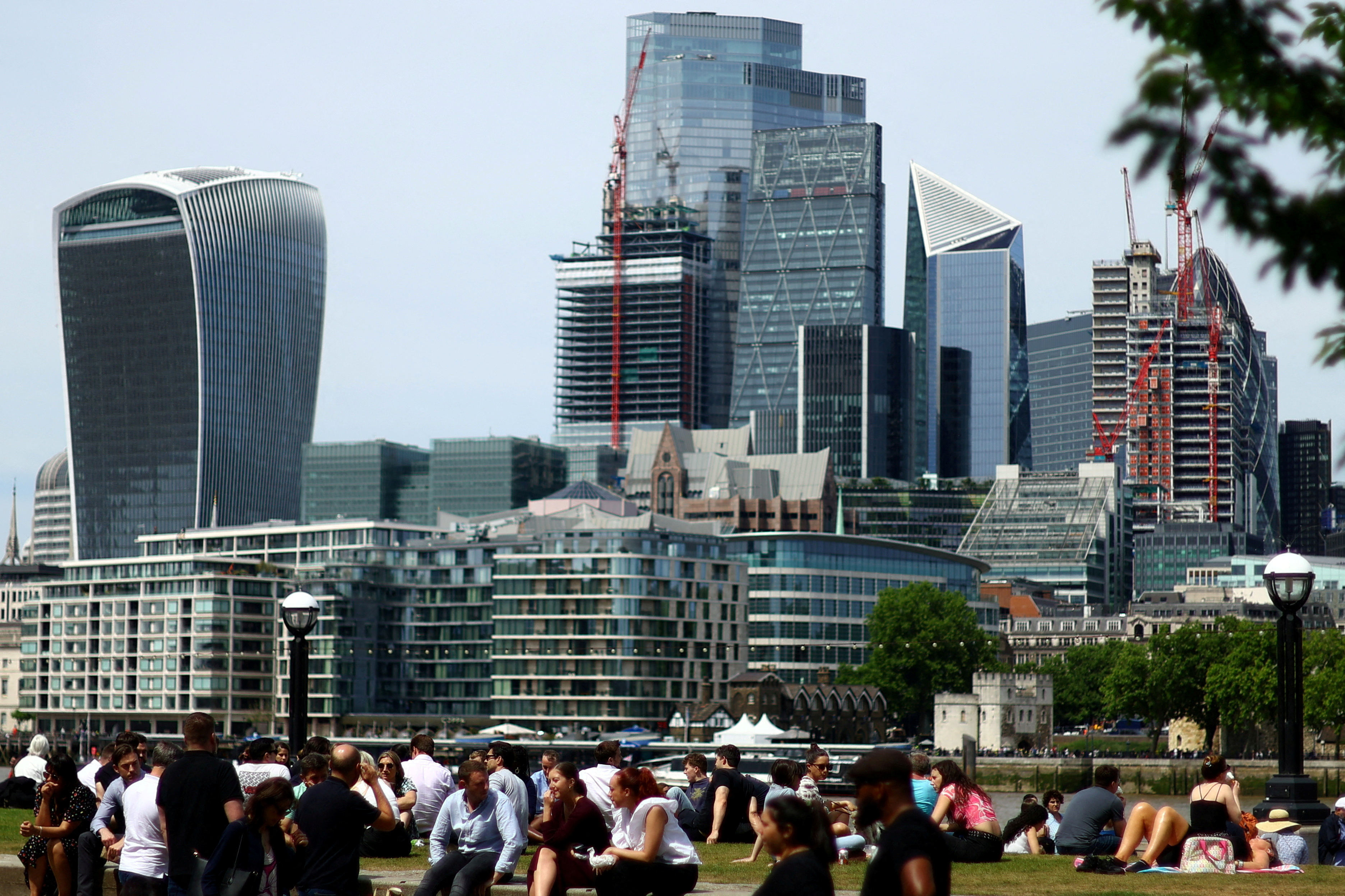 People enjoy warm weather in front of the city of London financial district in London