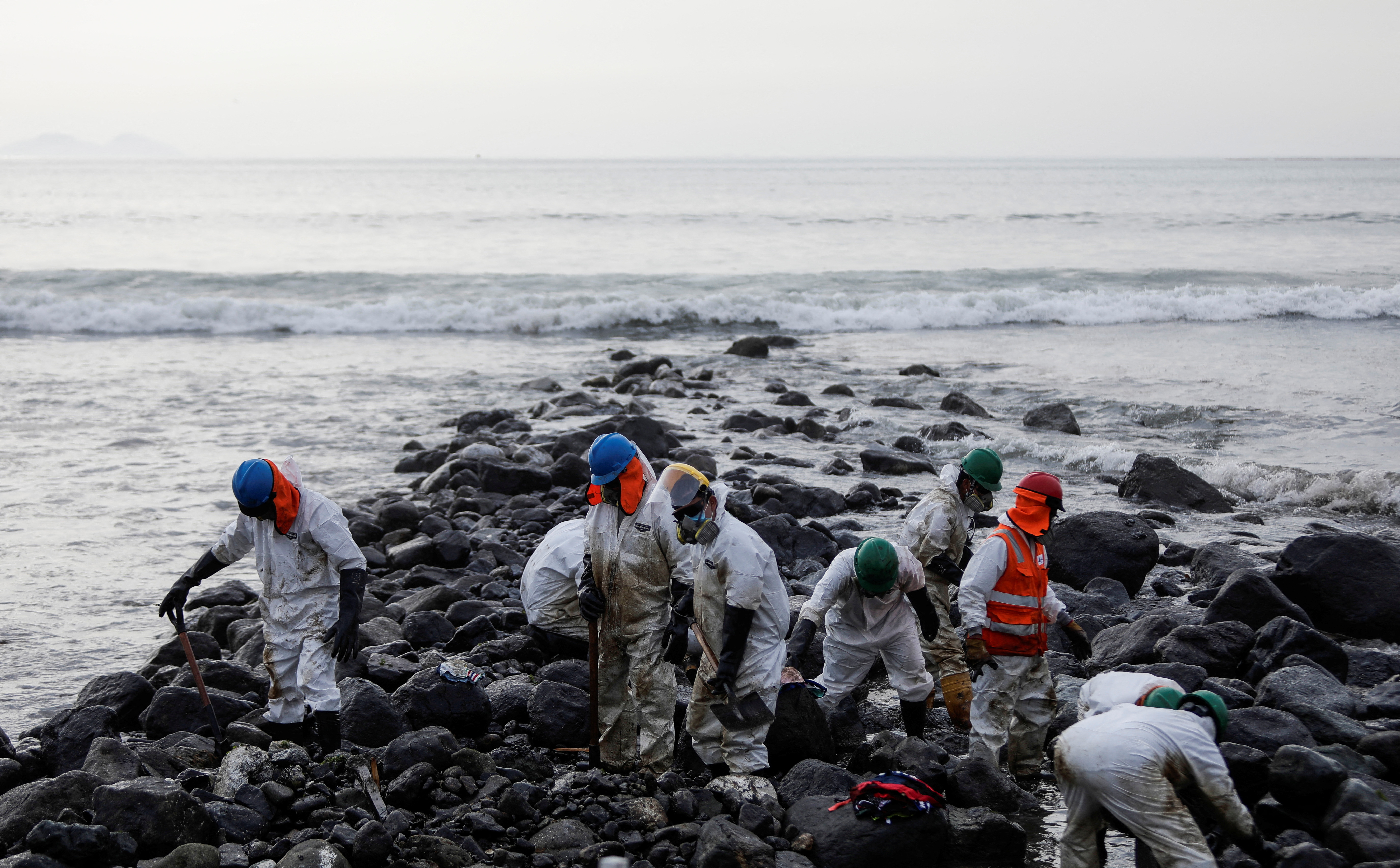Workers clean up an oil spill at the beach as demonstrators take part in a protest outside Repsol's La Pampilla refinery in Ventanilla