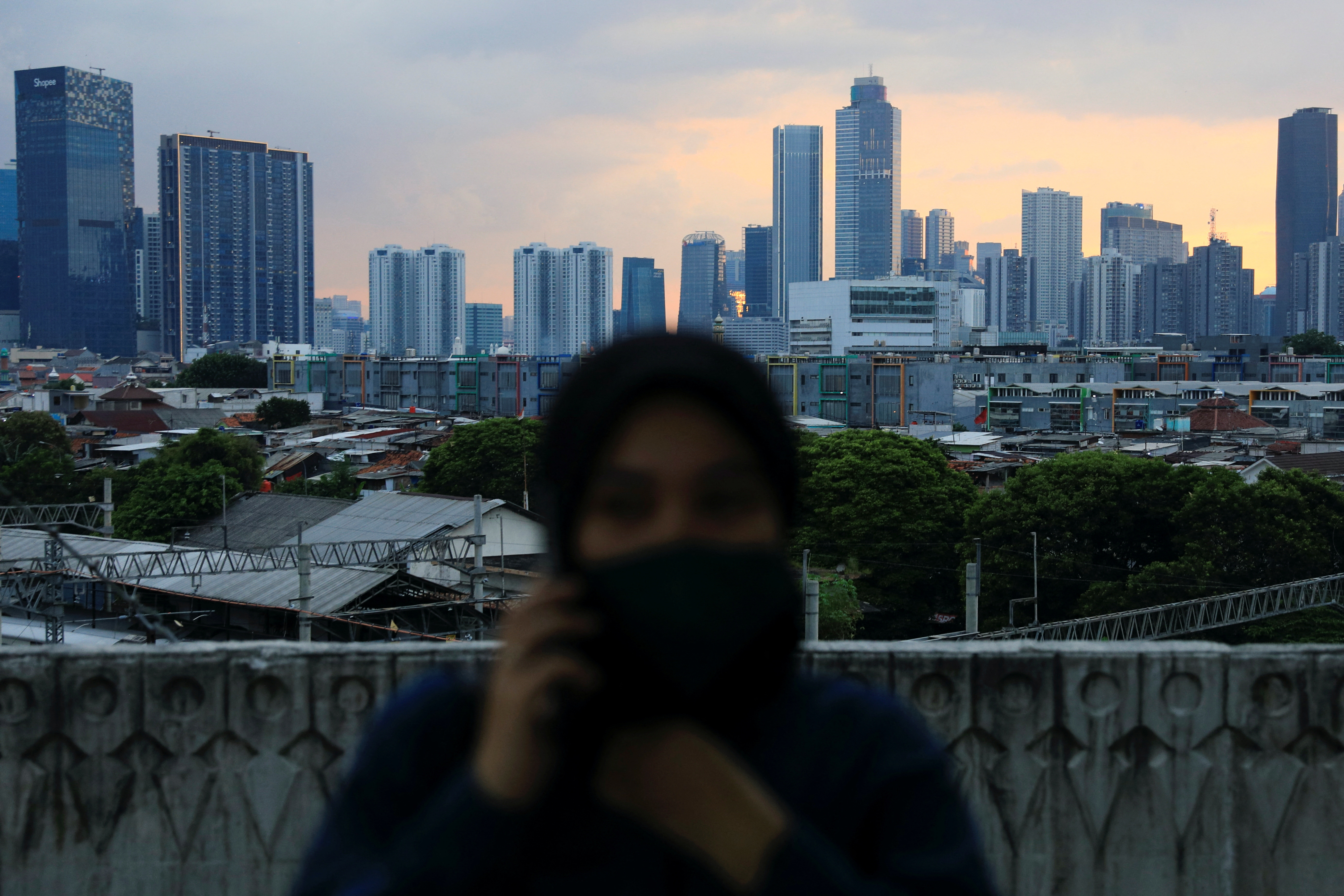 A woman uses her phone while waiting for a commuter train at a platform of station in Jakarta