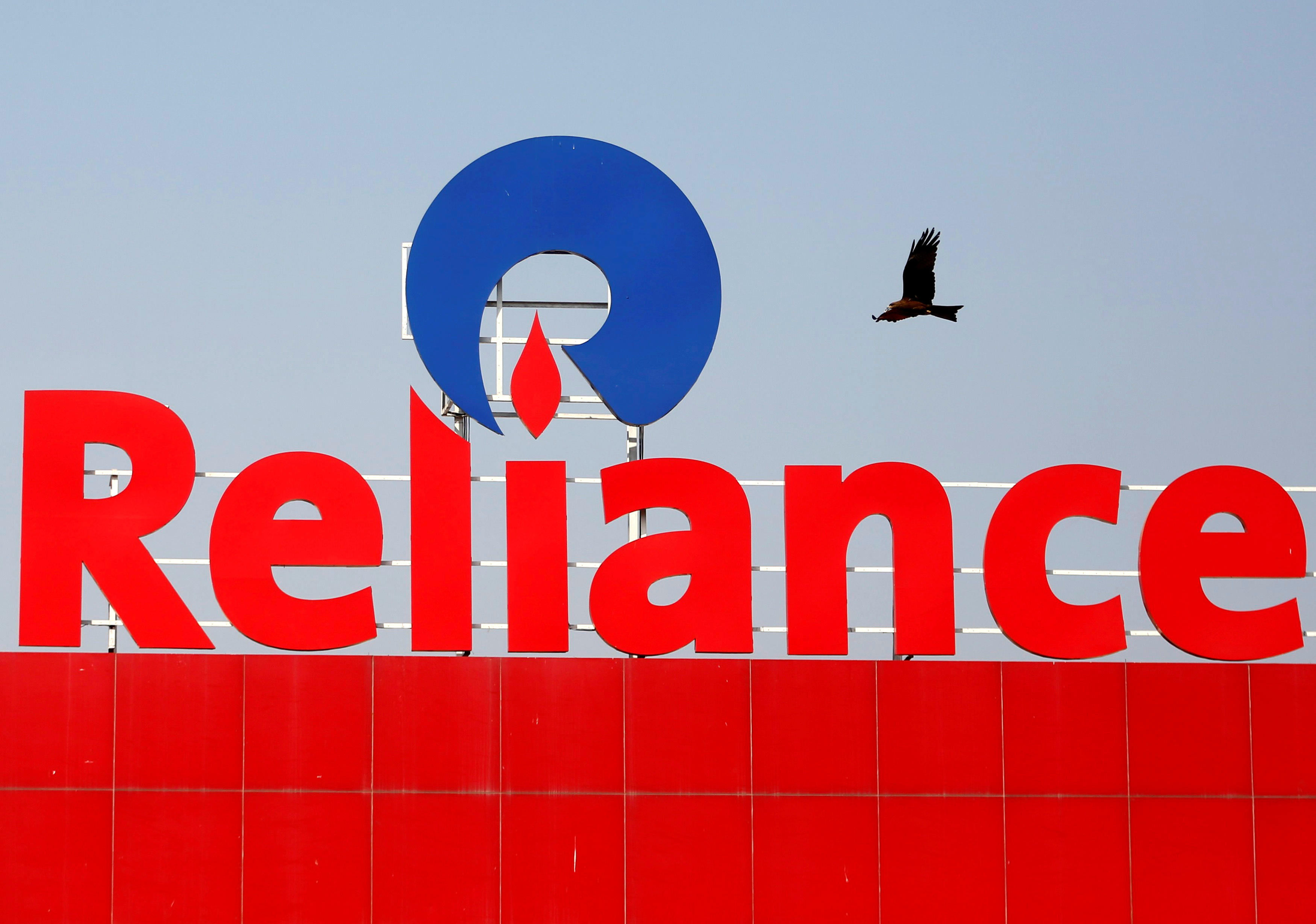 A bird flies past a Reliance Industries logo installed on its mart in Ahmedabad