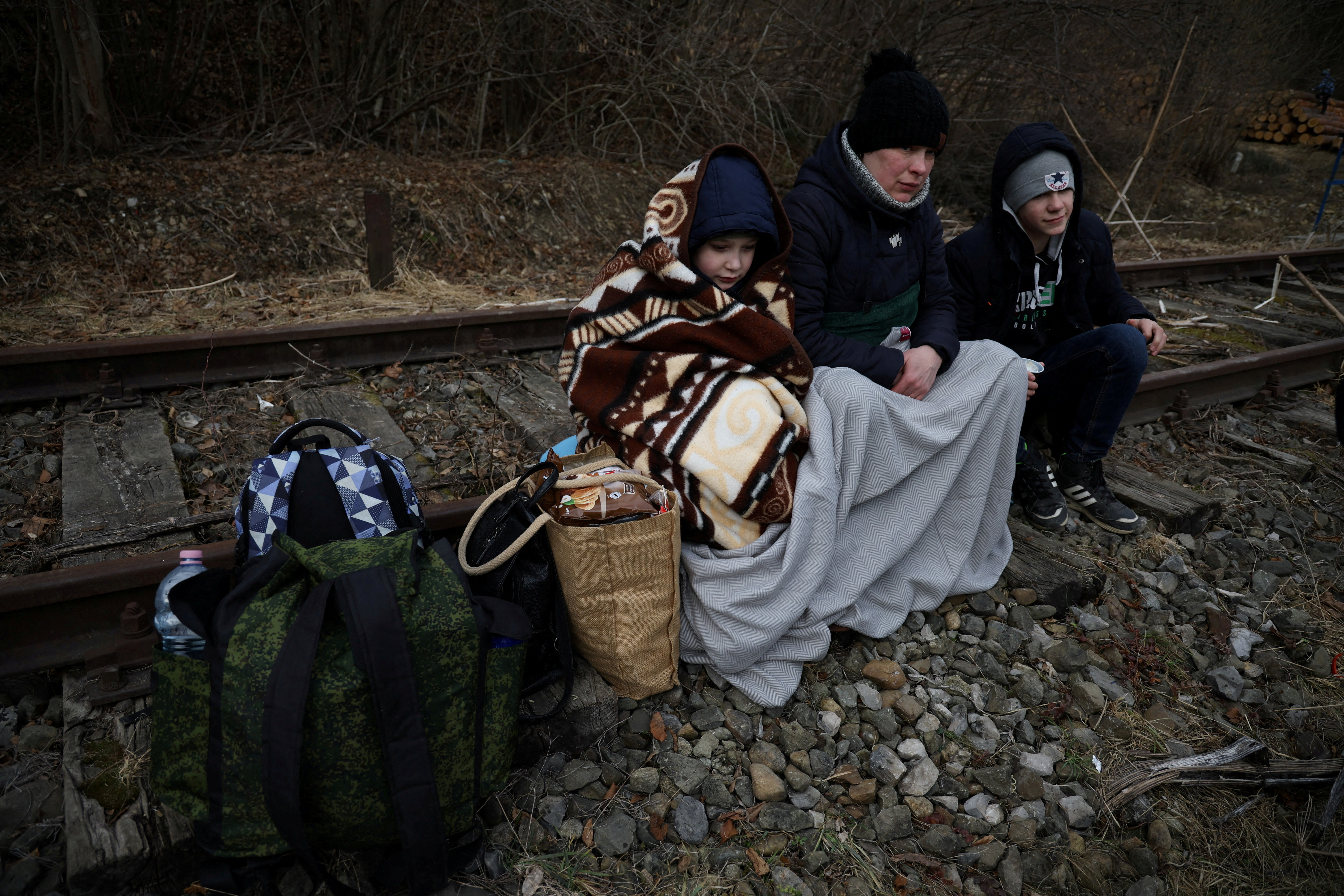 People sit on the railway after crossing the border between Poland and Ukraine, after Russia launched a massive military operation against Ukraine, in Kroscienko