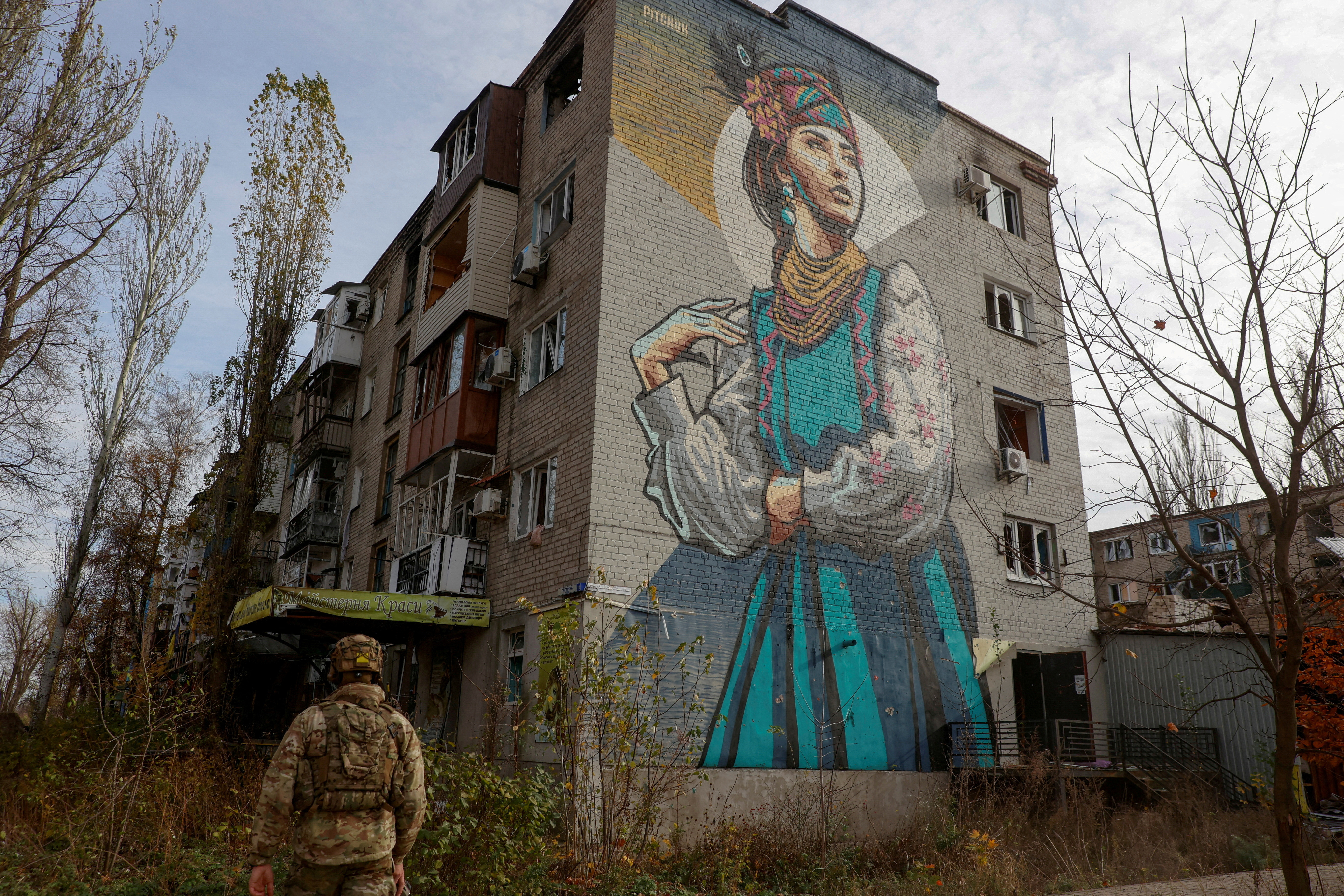 Ukrainian serviceman walks next to a residential building heavily damaged by permanent Russian military strikes in the front line town of Avdiivka