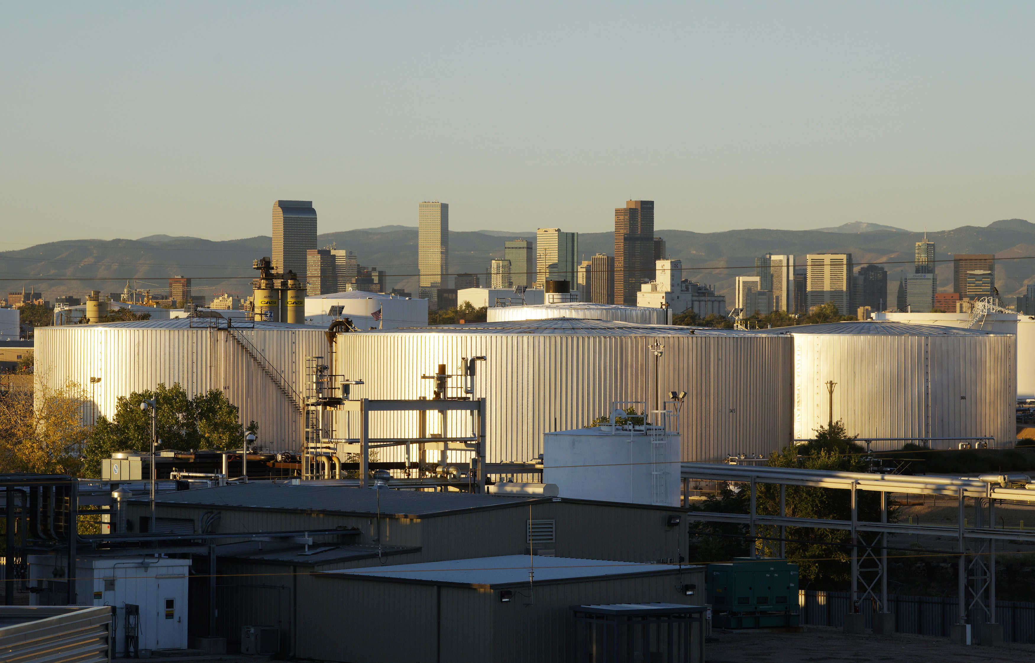Oil storage tanks are seen at sunrise with the Rocky Mountains and the Denver downtown skyline in the background