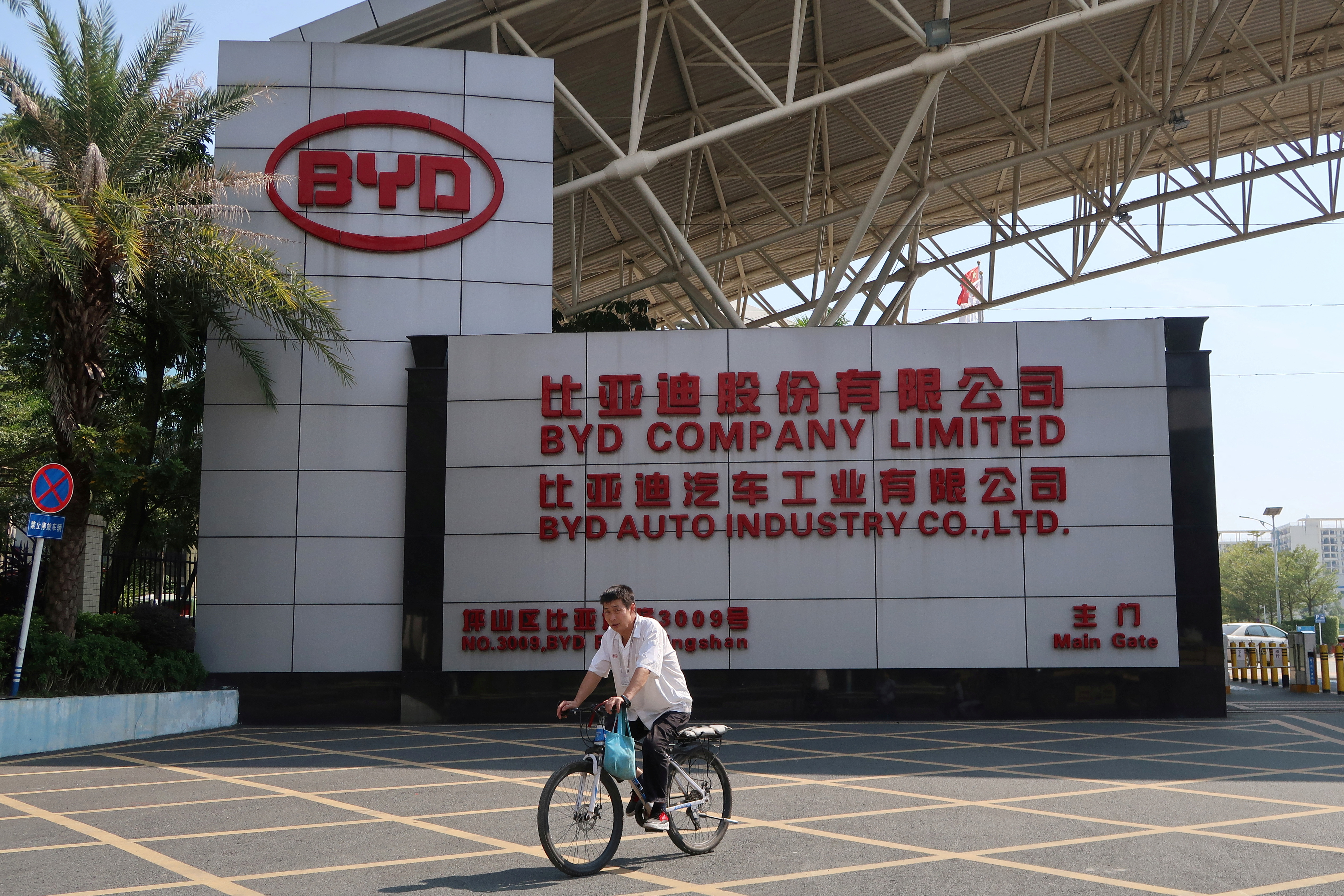 Man cycles past an entrance to the headquarters of Chinese electric car maker BYD in Shenzhen