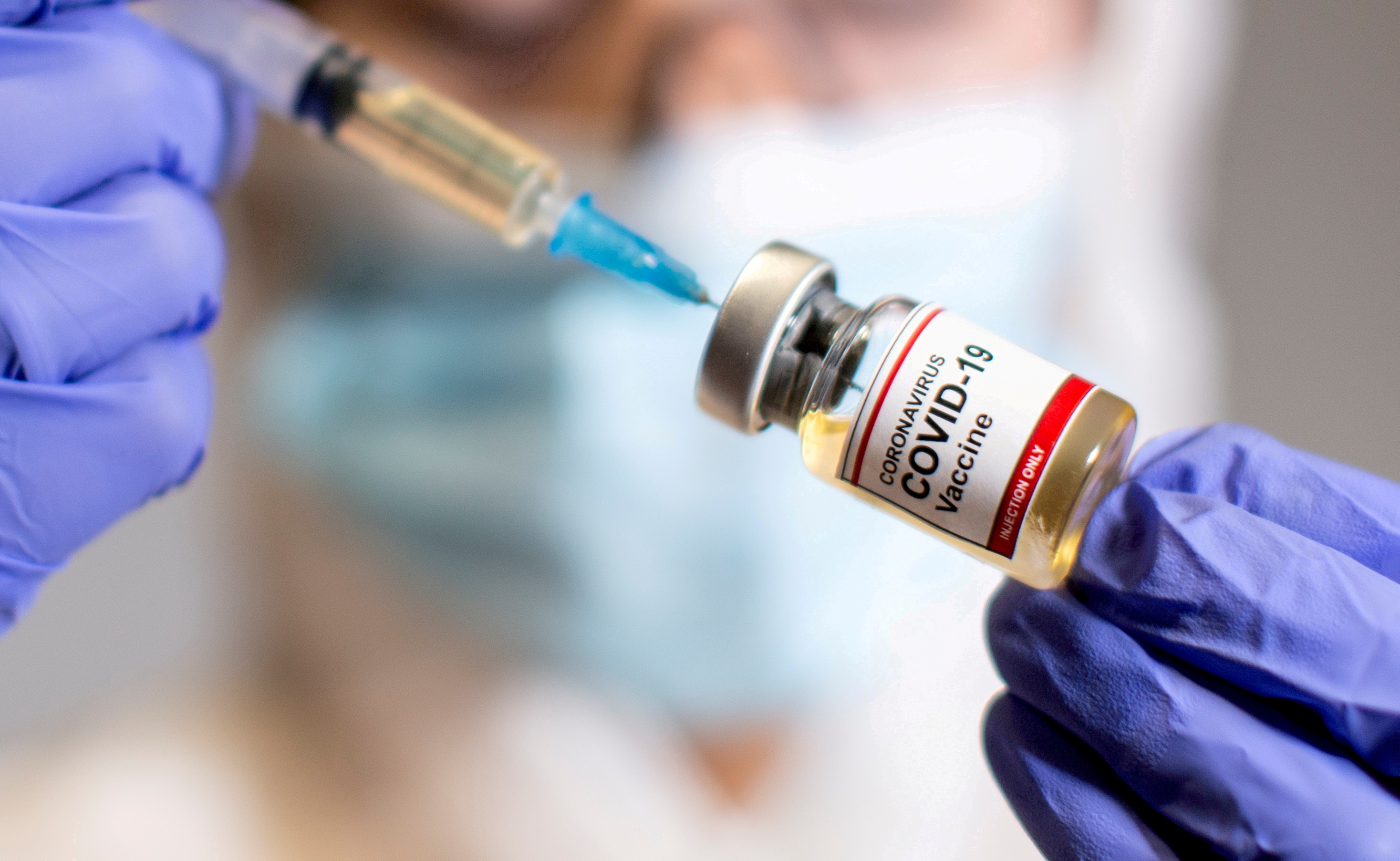 A woman holds a medical syringe and a small bottle labeled "Coronavirus COVID-19 Vaccine
