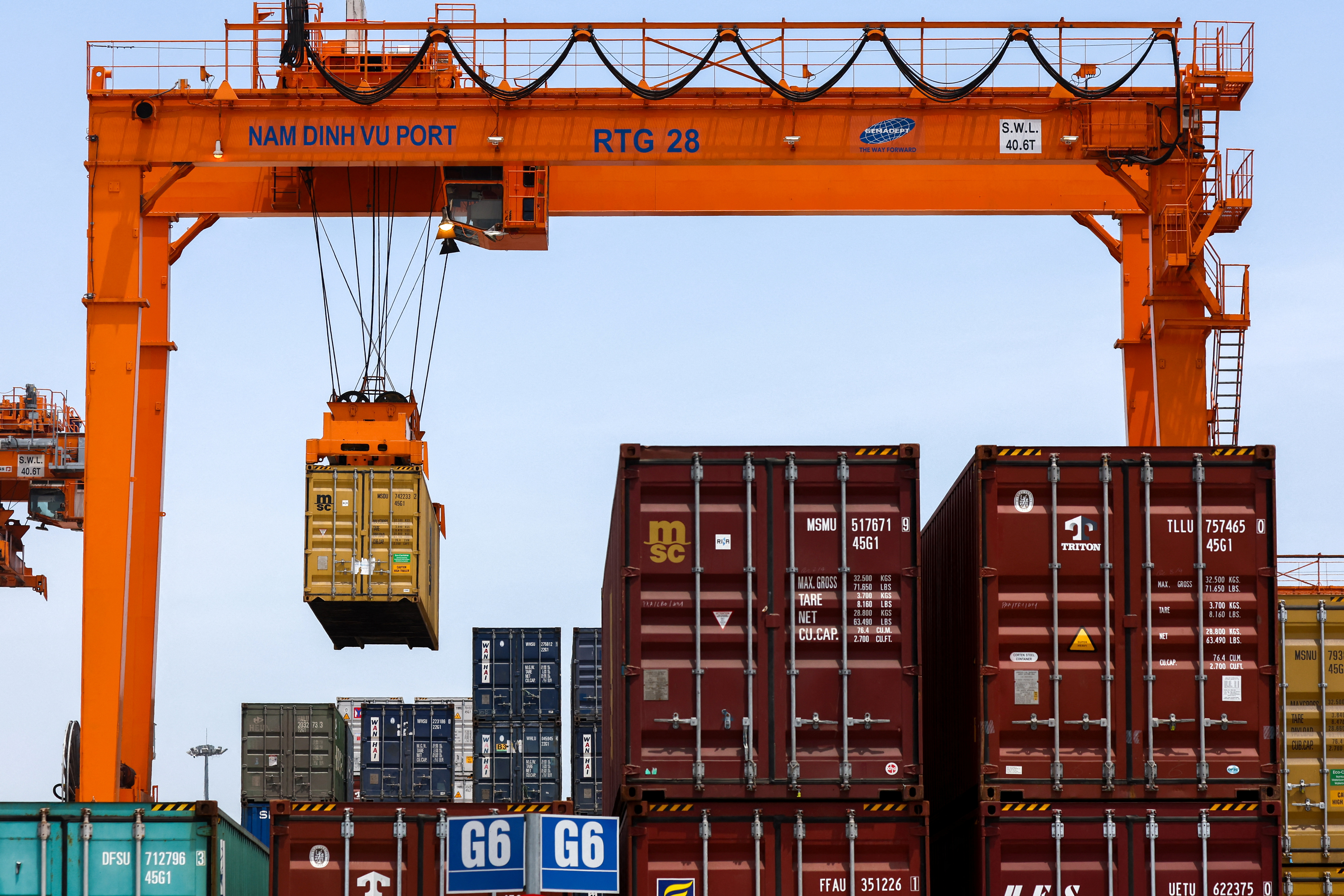 A large orange container crane labeled "NAM DINH VU PORT" hovers over stacked shipping containers at a port scene.