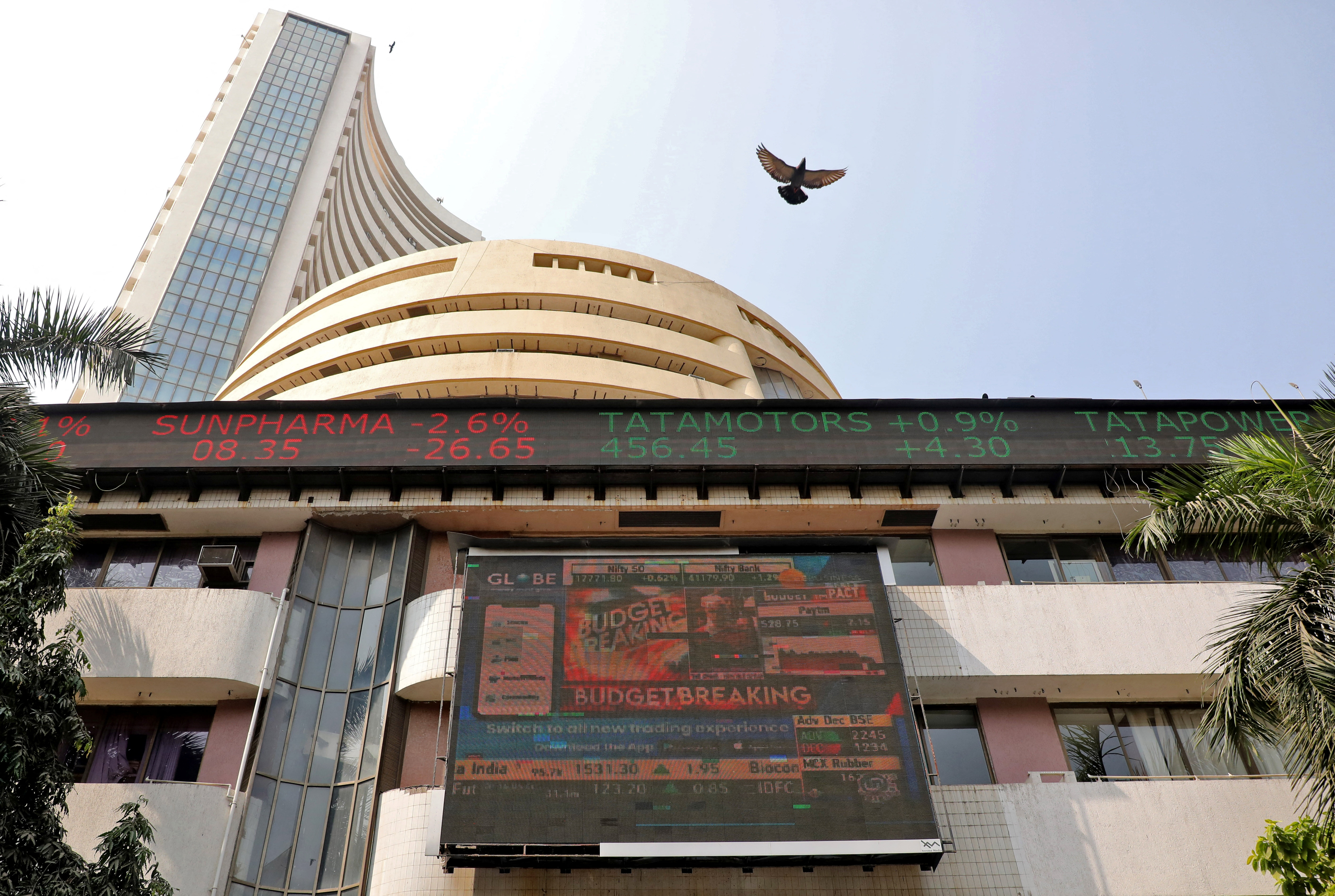 A bird flies past a screen displaying the Sensex results on the facade of BSE building in Mumbai