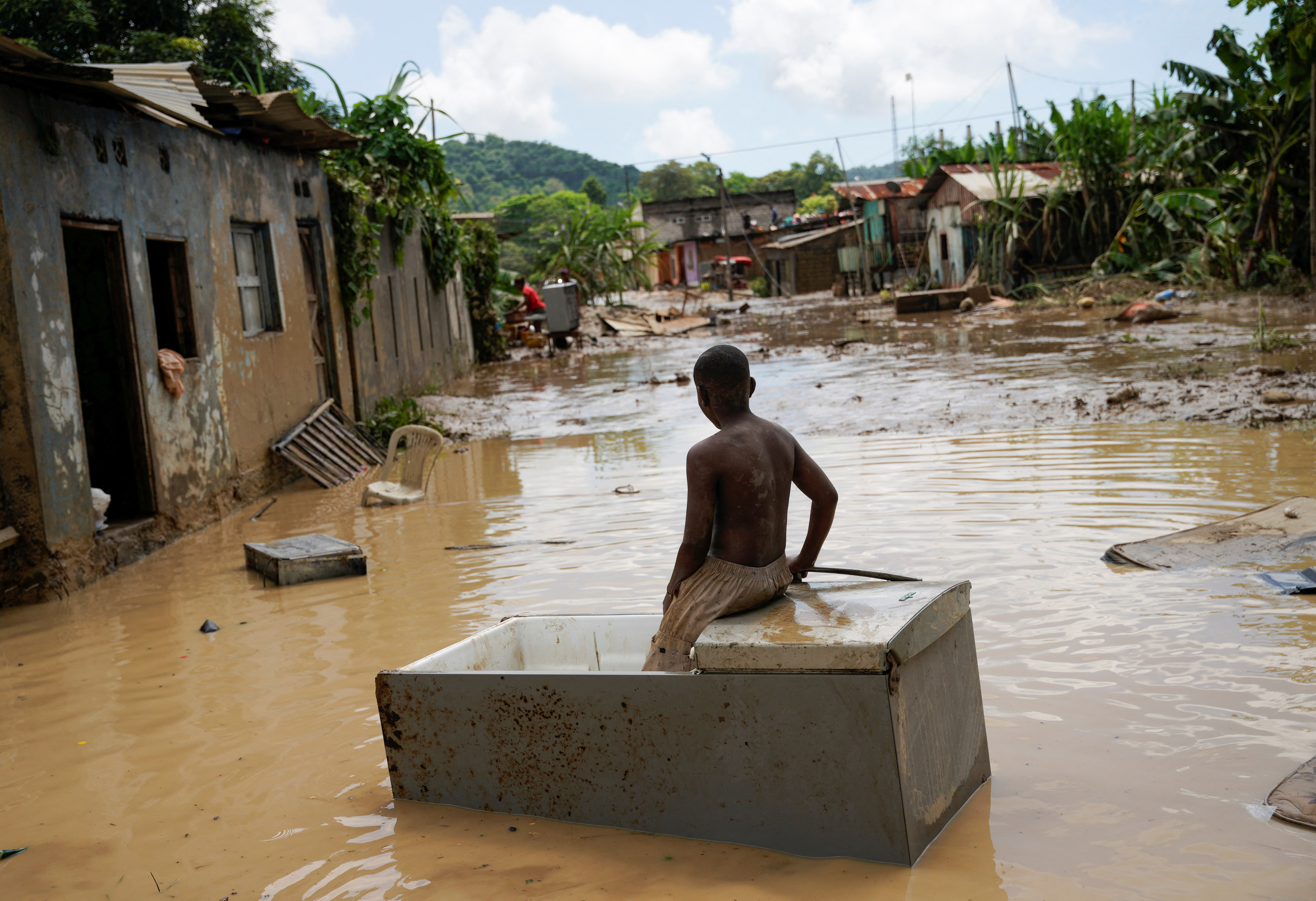 A boy sits on a refrigerator surrounded by floodwater.