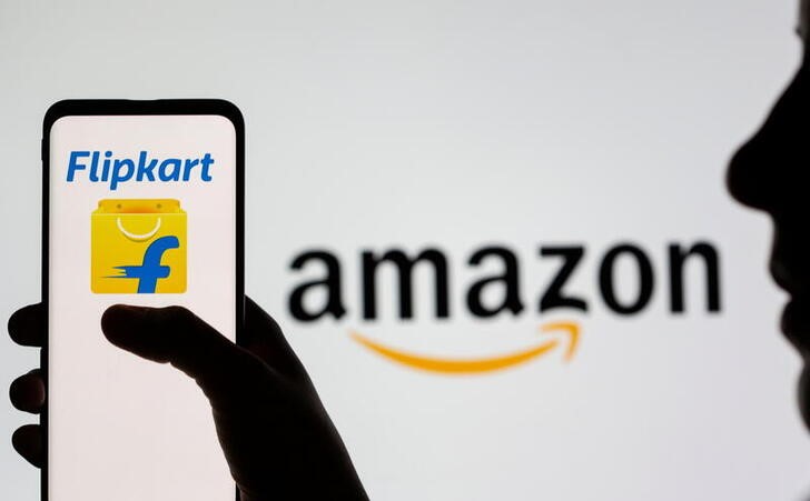 Woman holds smartphone with Flipkart logo in front of displayed Amazon logo in this illustration taken