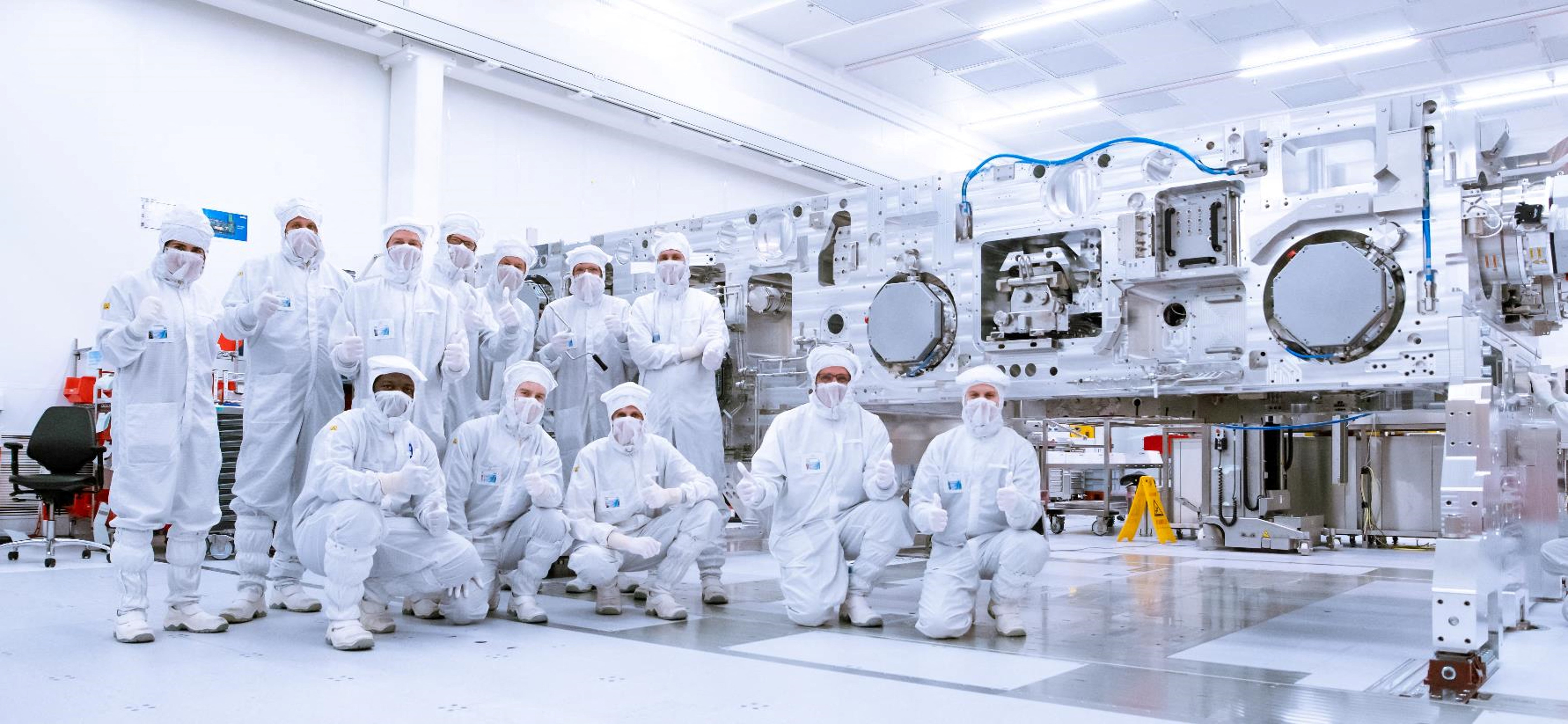 ASML employees pose in front of the partially completed frame of the company’s newest product