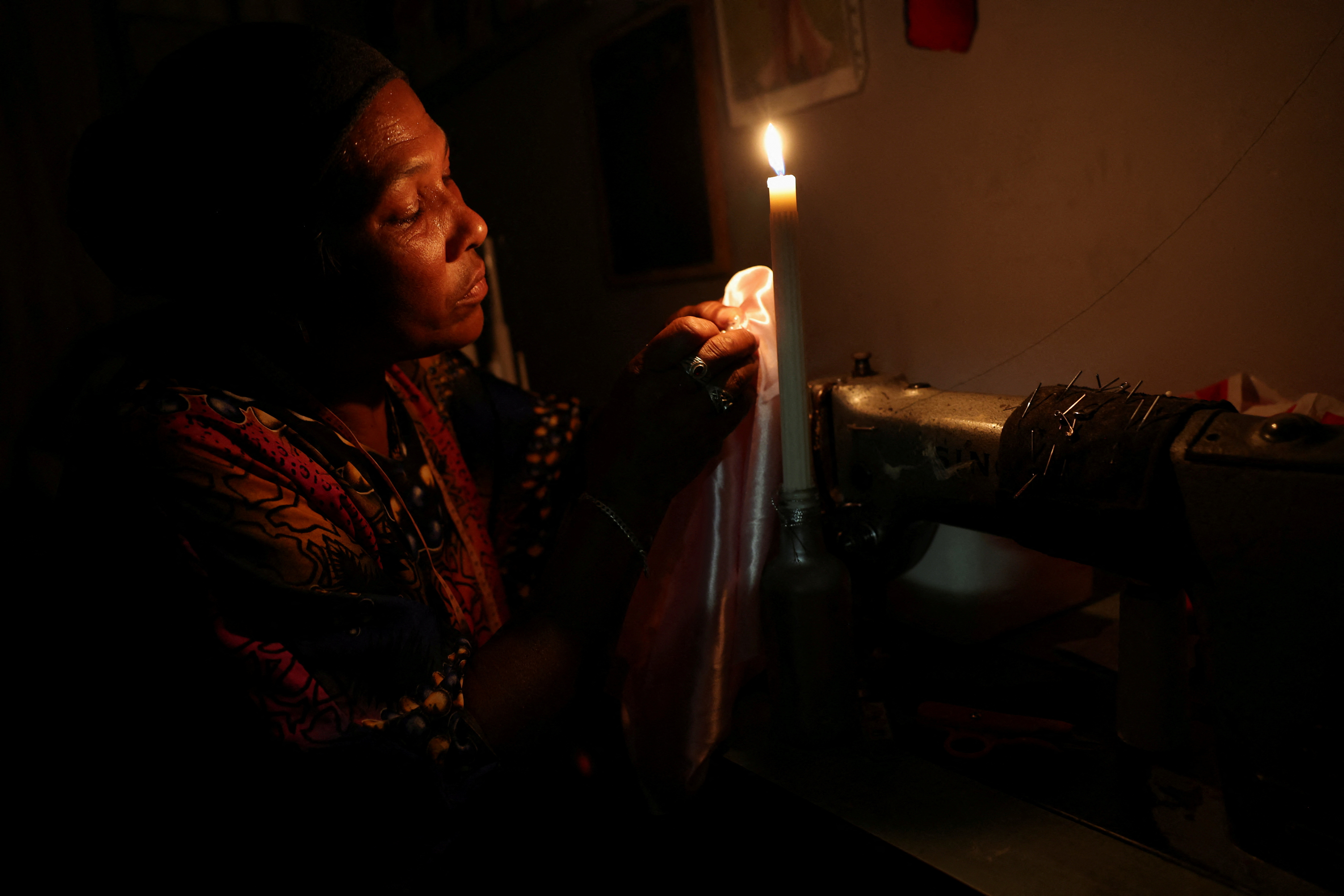 Dressmaker Faieza Caswell from Mitchells Plain sews under candlelight in her workplace, in Cape Town